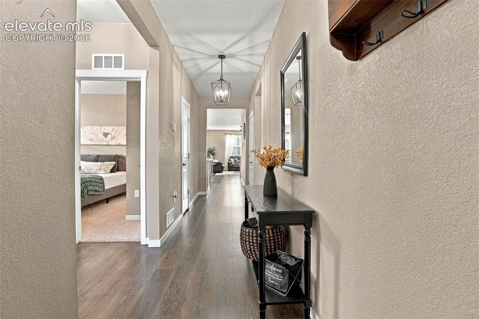 Hallway featuring wood-finish flooring, textured wall finishes, and a hanging metal-frame lantern pendant light