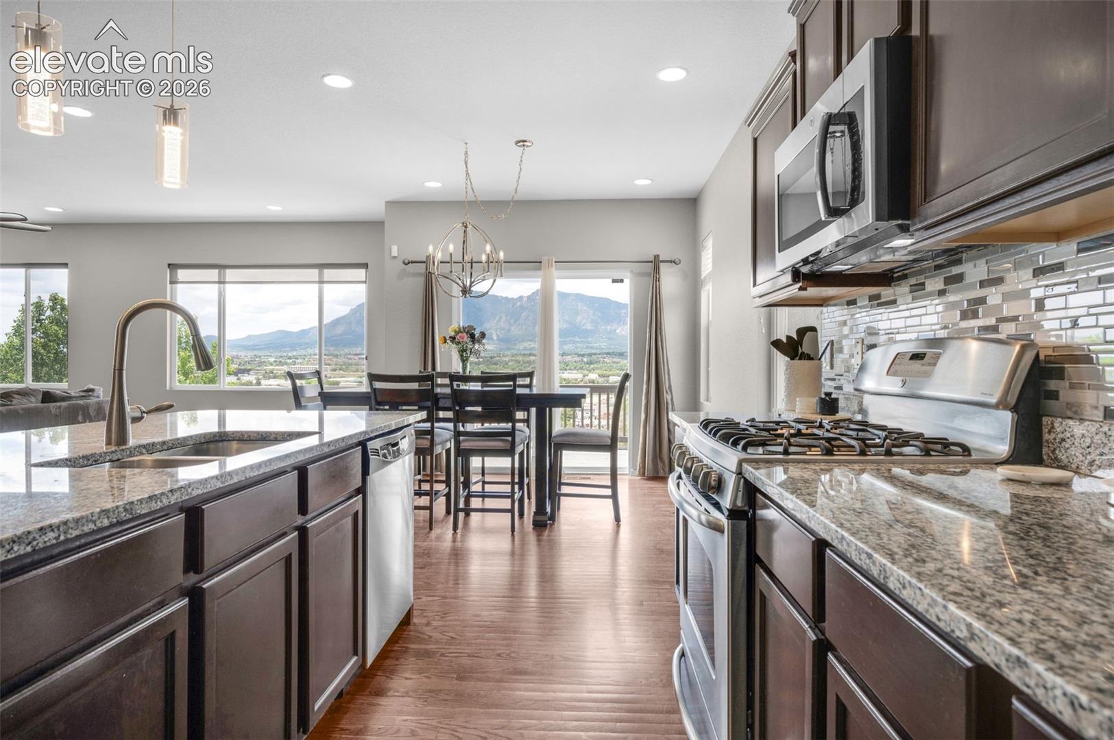 Modern kitchen featuring dark wood cabinetry, stainless steel appliances, granite countertops, and a tiled backsplash. Fantastic view of the front range
