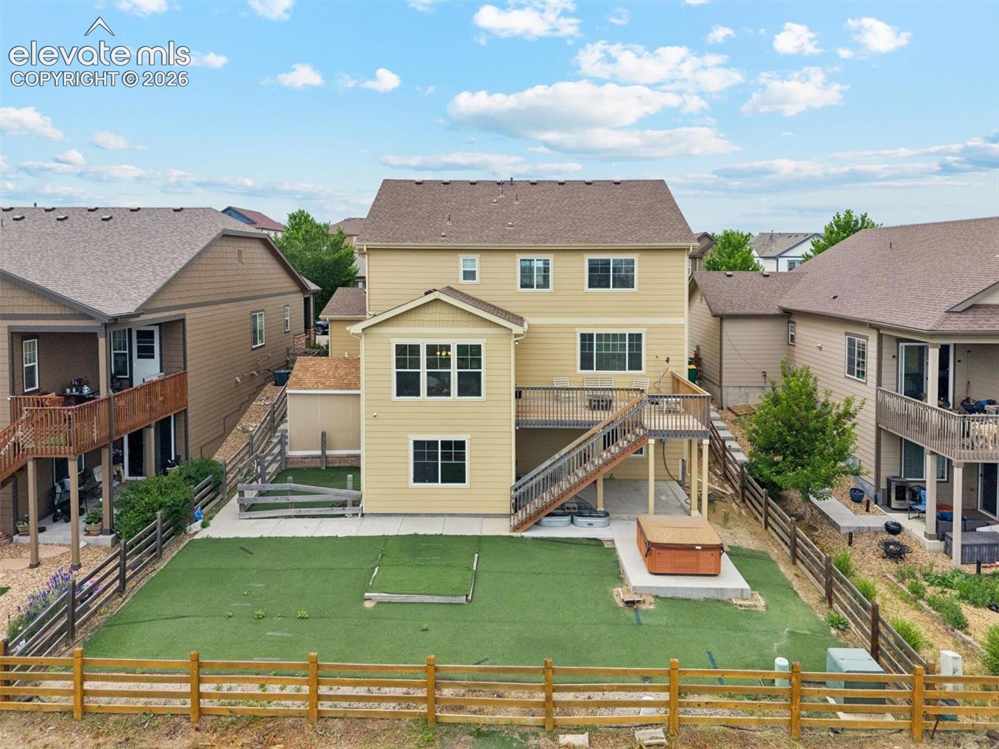 Rear exterior featuring a multi-level deck, a hot tub on a concrete pad, and a fenced yard with artificial turf