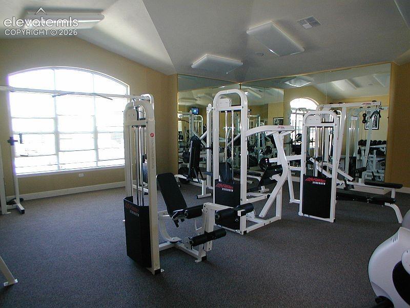 Fitness area featuring vaulted ceilings, large arched window, wall-to-wall mirrors, and neutral carpet flooring