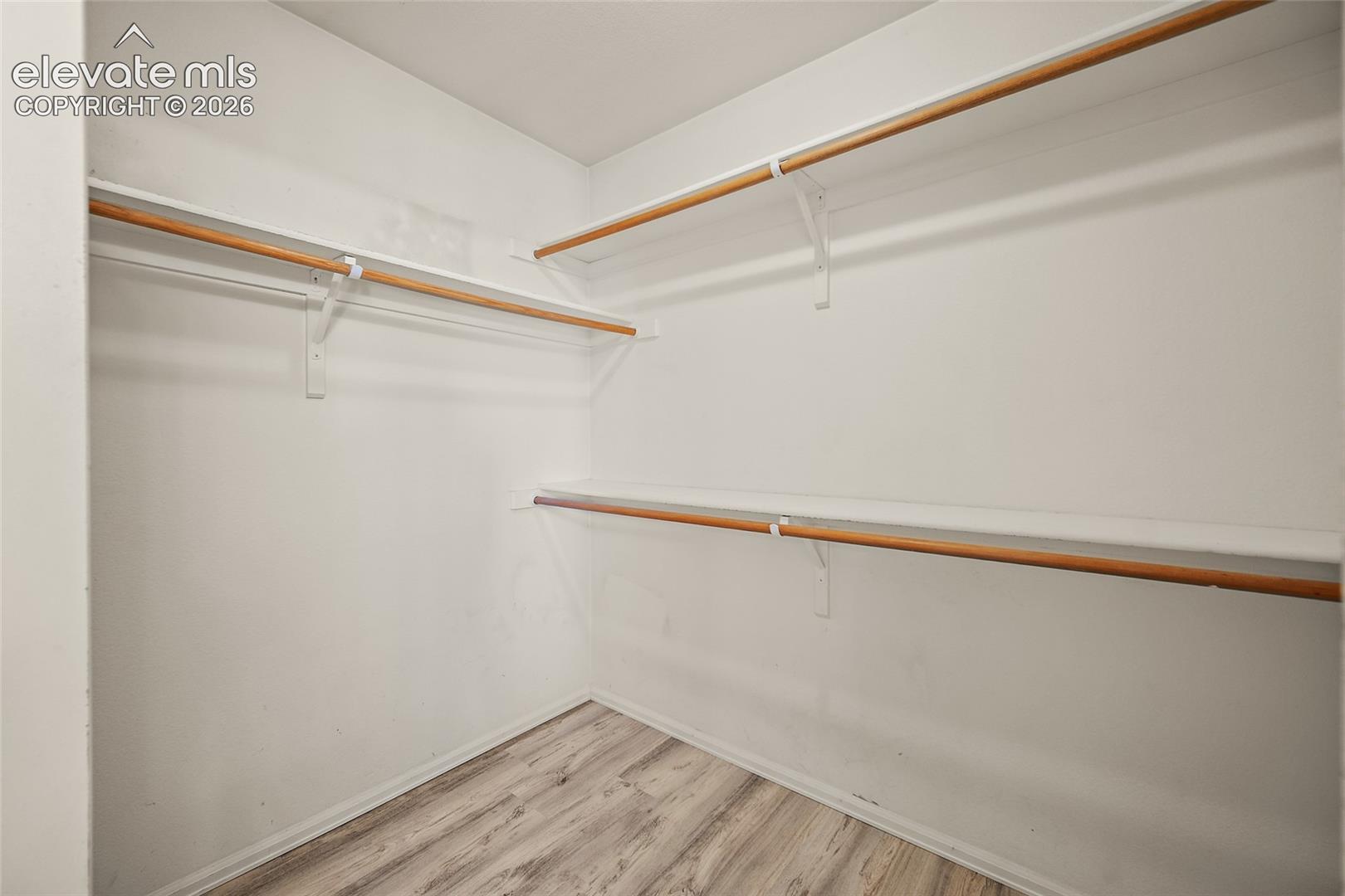 Spacious closet featuring white walls, multi-level shelving, wood-finish flooring, and ample hanging rods