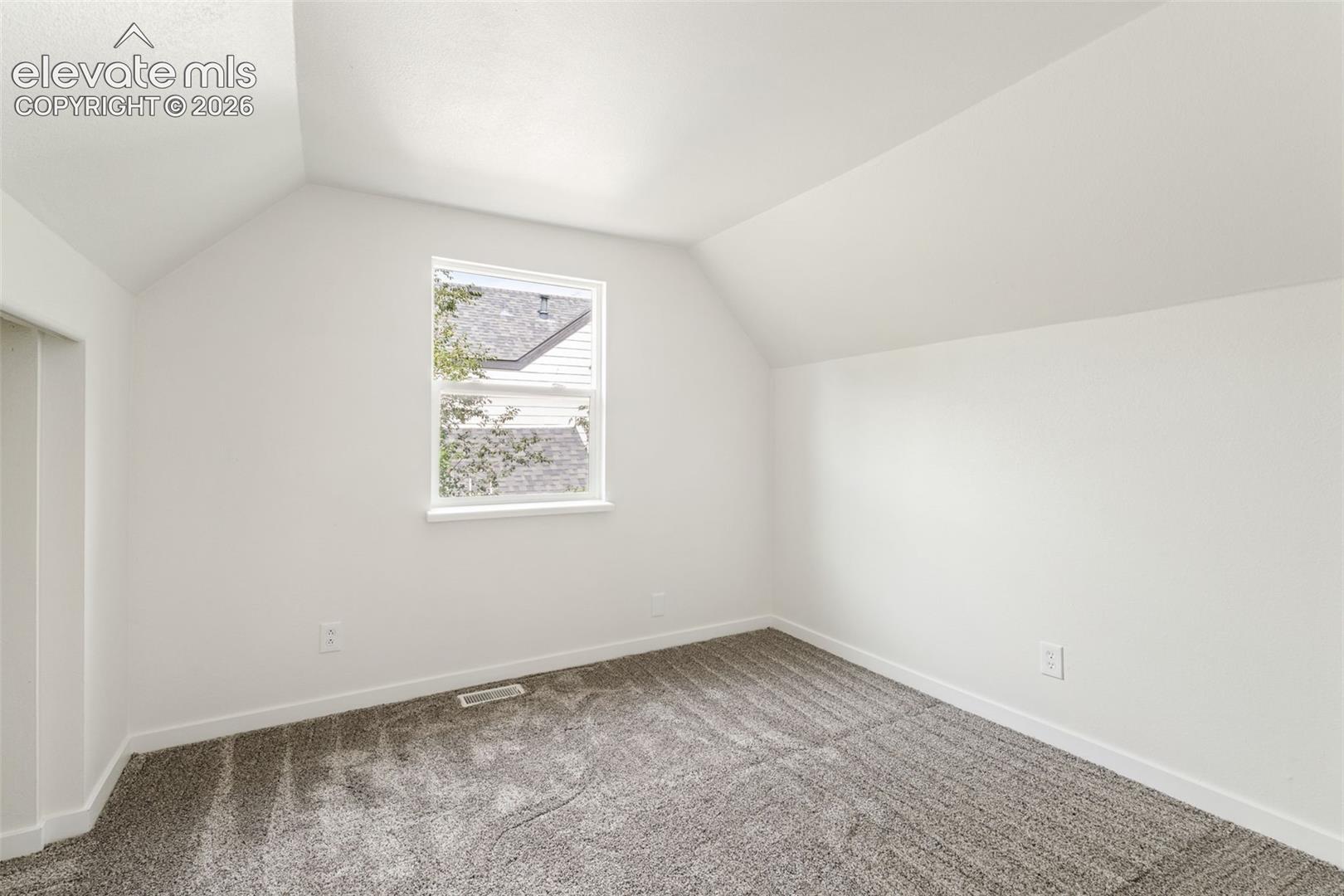 Interior room featuring neutral wall-to-wall carpeting, angled ceiling lines, and a single-pane window