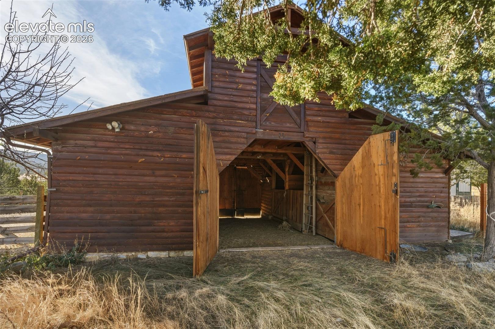 Barn structure featuring log siding, a gambrel roof, and large wooden doors