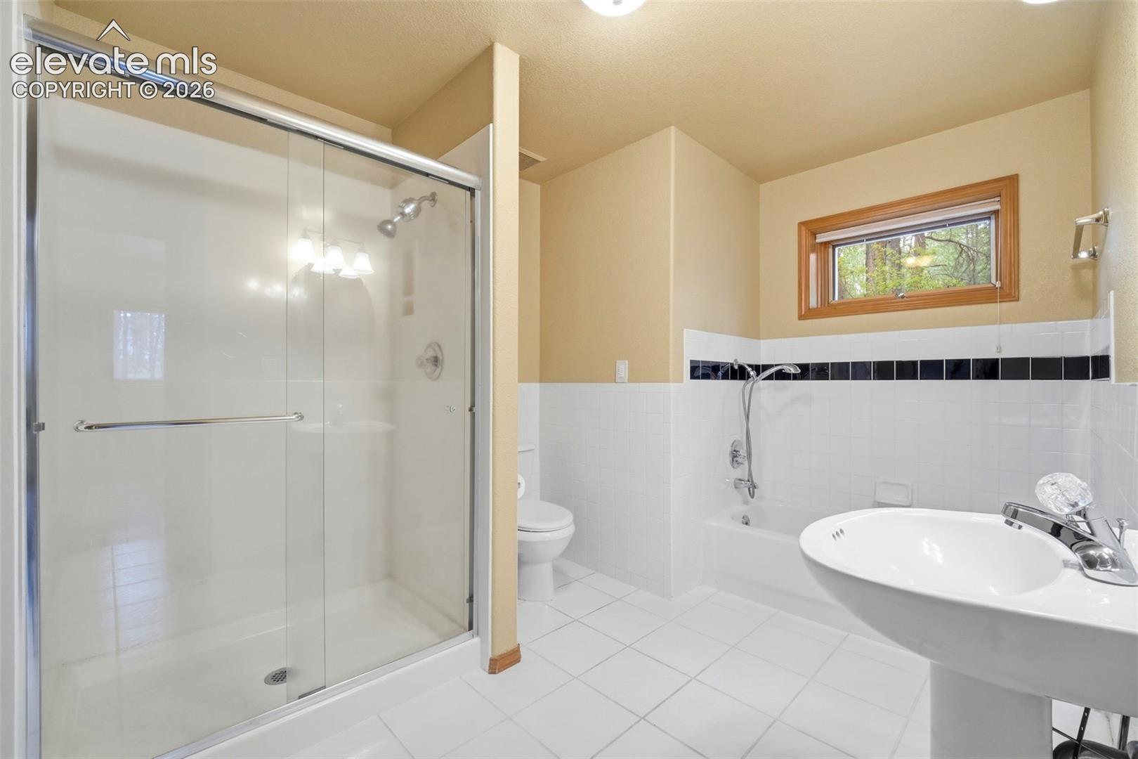 Bathroom featuring a glass-enclosed shower, pedestal sink, and a combination tub/shower with a tiled surround