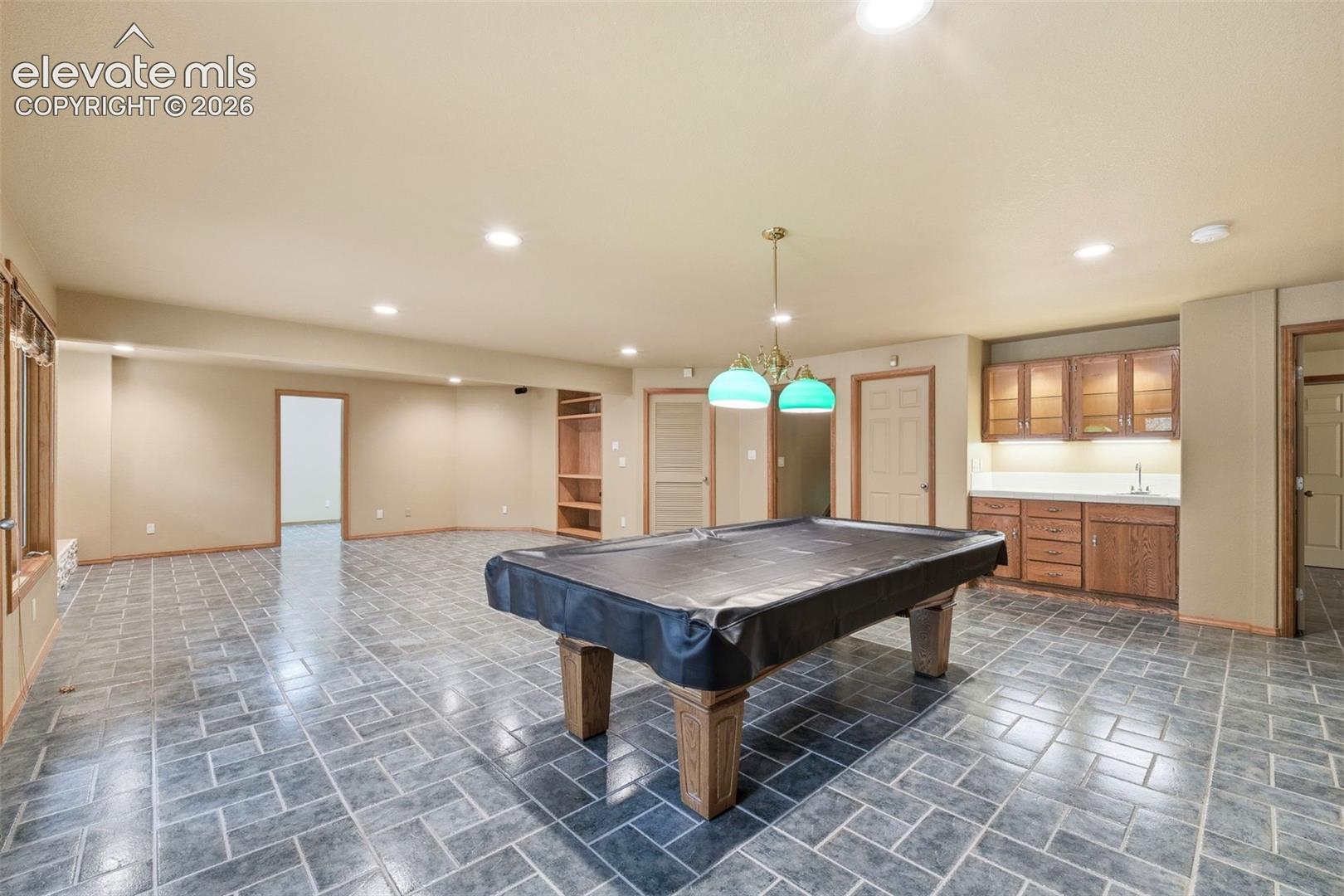 Spacious recreation room featuring robust tile flooring, a built-in wet bar with cabinetry and sink, recessed lighting, and an additional pendant light fixture