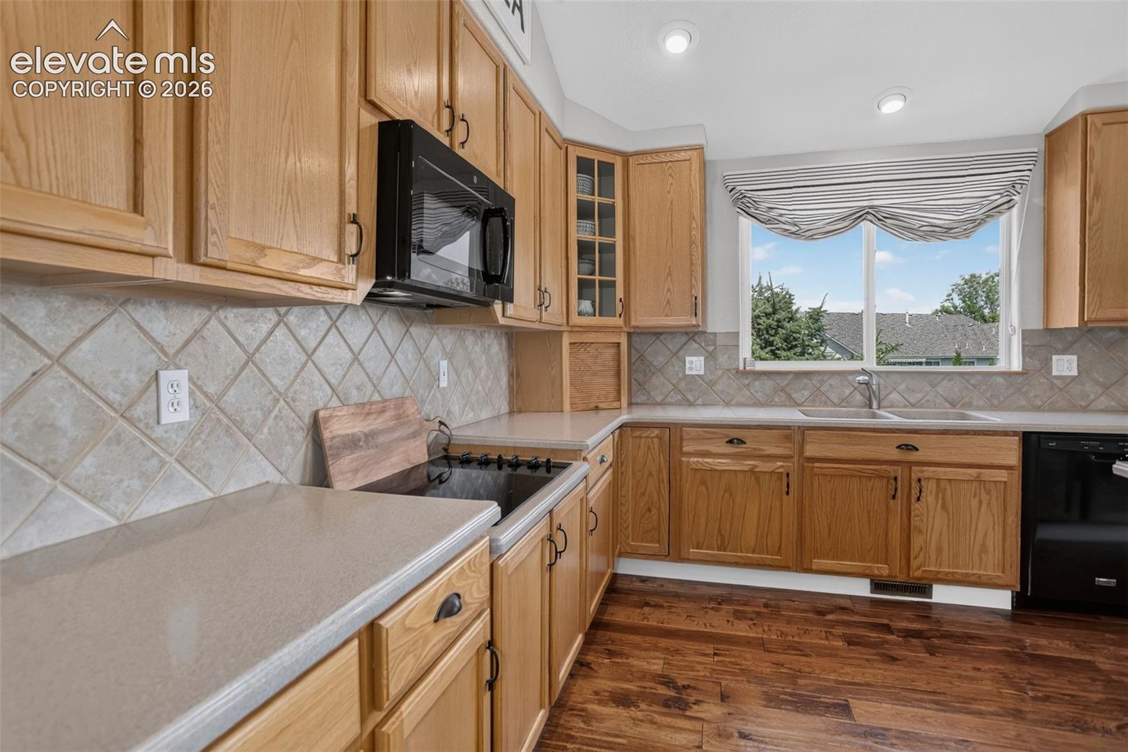 Kitchen featuring light wood-finish cabinetry, light-toned countertops, a tile backsplash, and wood-finish flooring