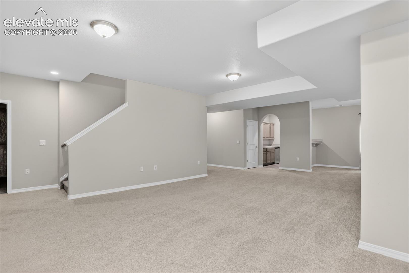 Spacious room featuring neutral carpet flooring, recessed lighting, and a partial staircase with white risers and handrails