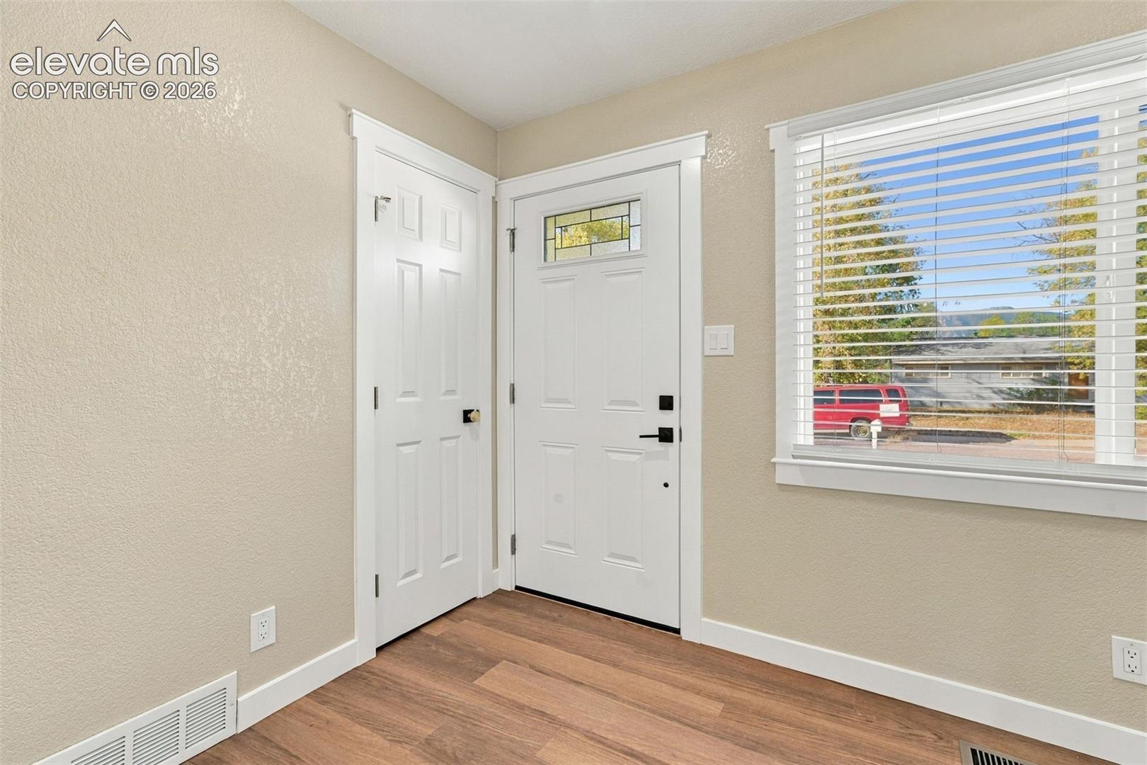 Entryway featuring wood-finish flooring, a six-panel interior door, and an exterior door with an upper decorative glass inlay and matte black hardware