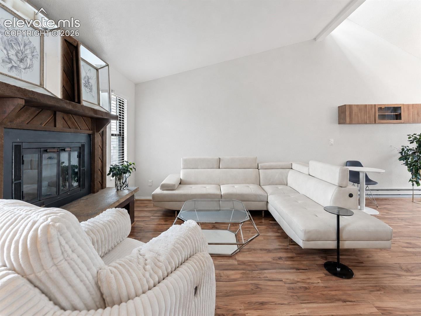Vaulted ceiling, wood-finish flooring, wood-clad fireplace, and built-in floating cabinetry