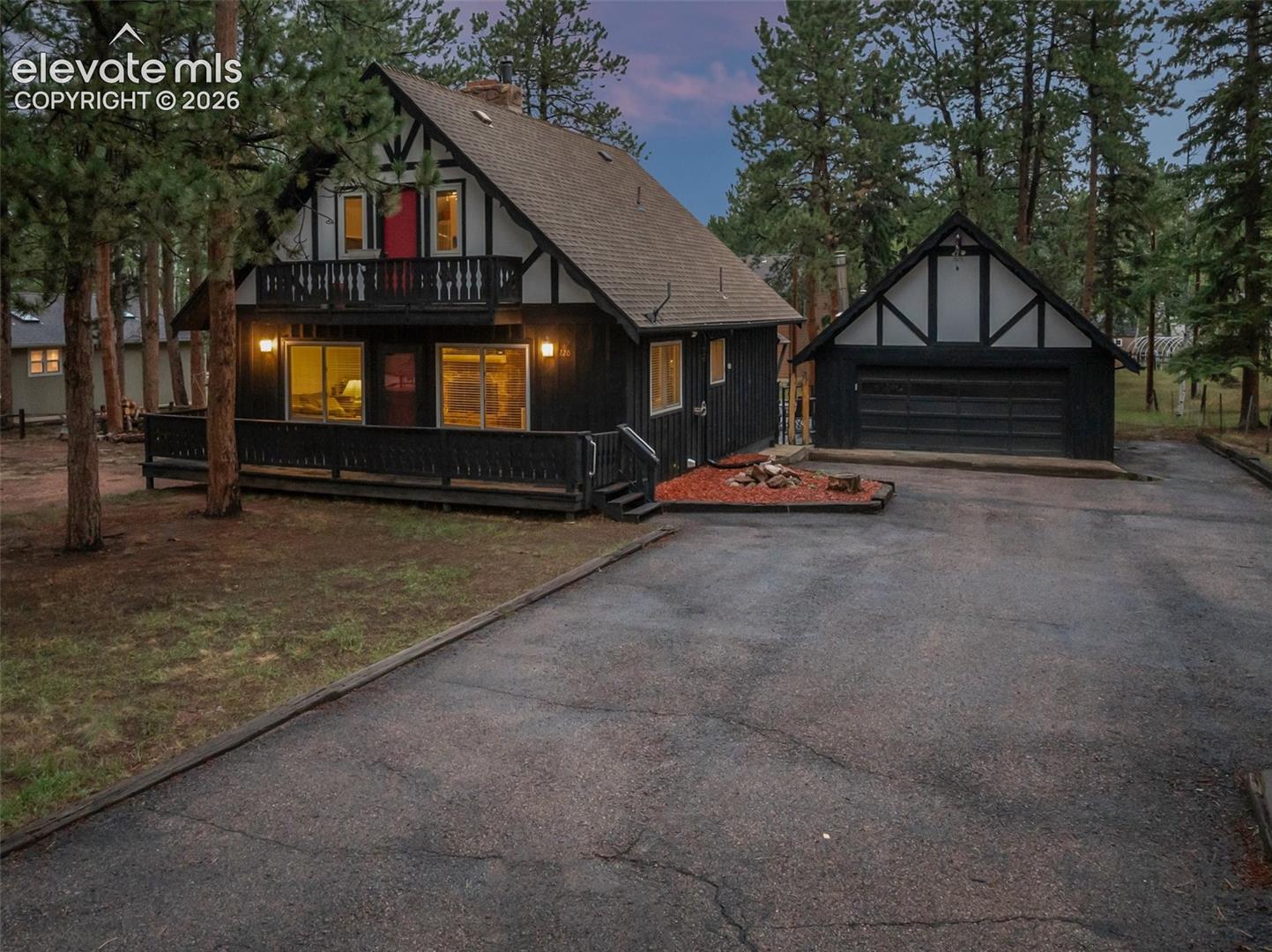 Tudor-style exterior with dark siding and white trim accents, featuring a prominent balcony, an attached covered porch, a separate two-car garage, and a paved driveway