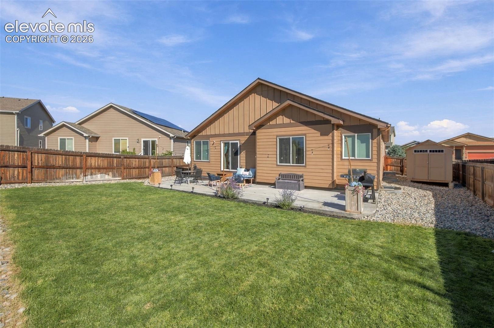 Rear exterior featuring horizontal and vertical wood-style siding, concrete patio, fenced backyard, manicured lawn, and detached storage shed