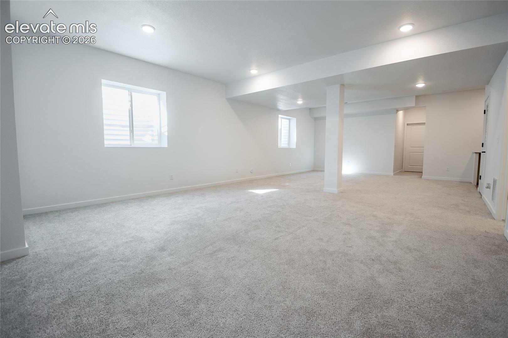 Open-concept interior space featuring neutral wall-to-wall carpeting, recessed ceiling lighting, and dual inset windows