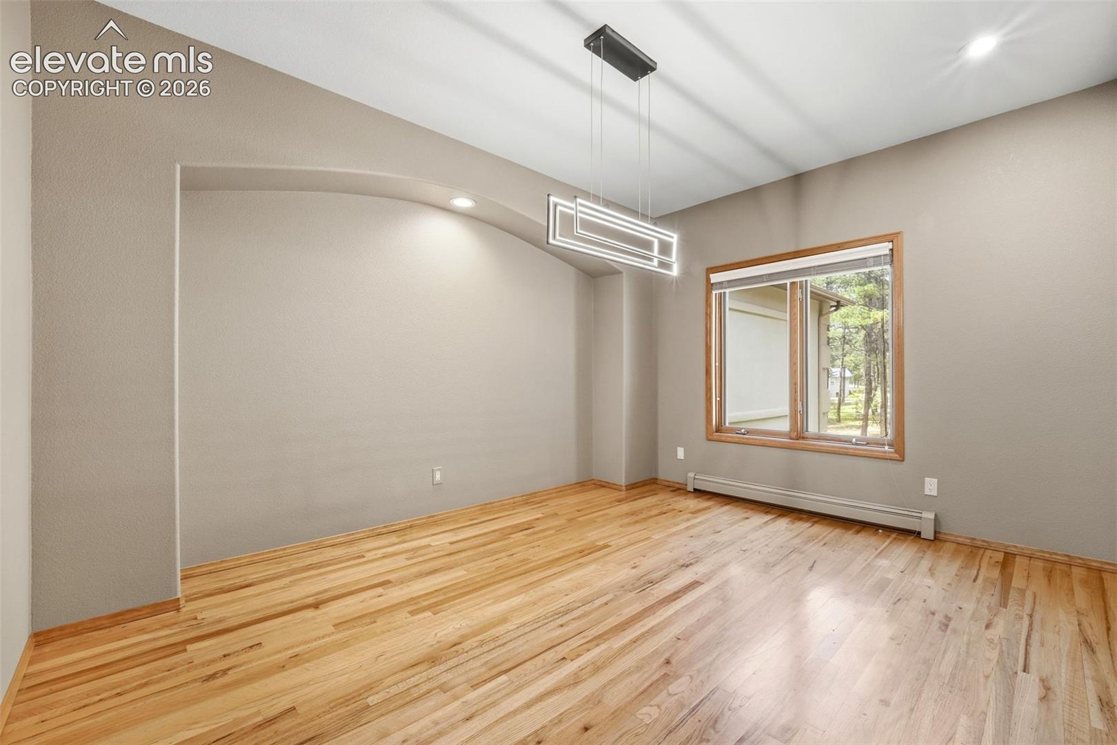 Spacious room featuring wood-finish flooring, a modern linear chandelier, an arched wall niche with recessed lighting, and a large window with natural wood trim