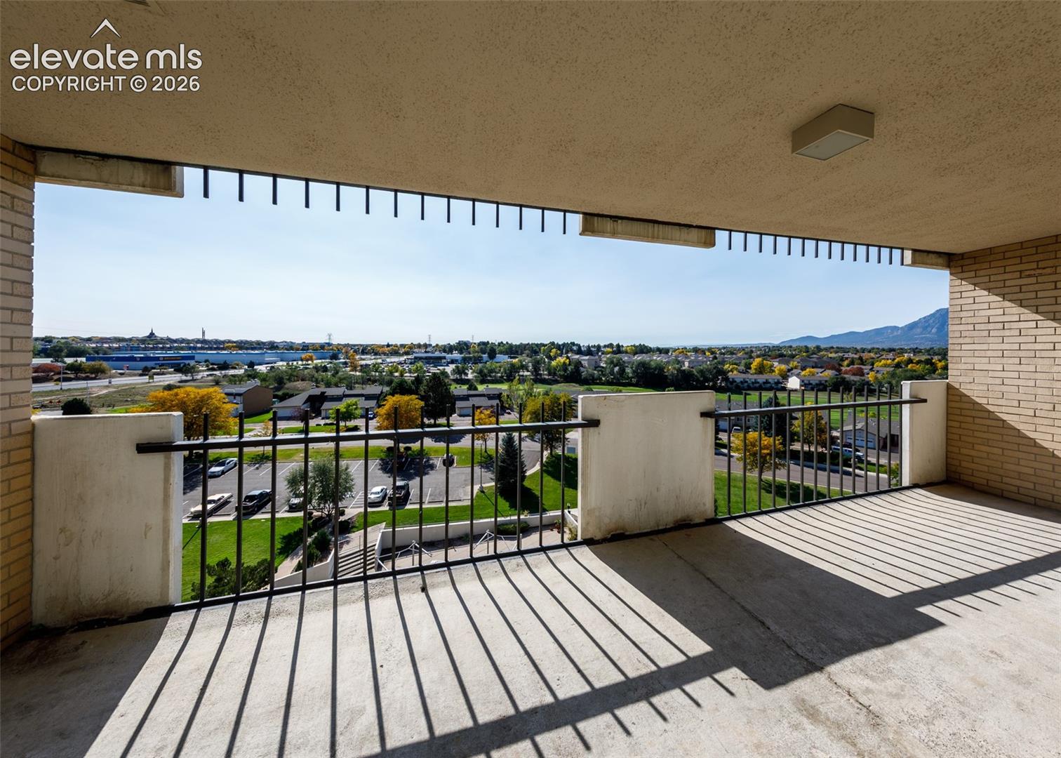 Covered balcony with brick side walls, concrete flooring, and metal railing