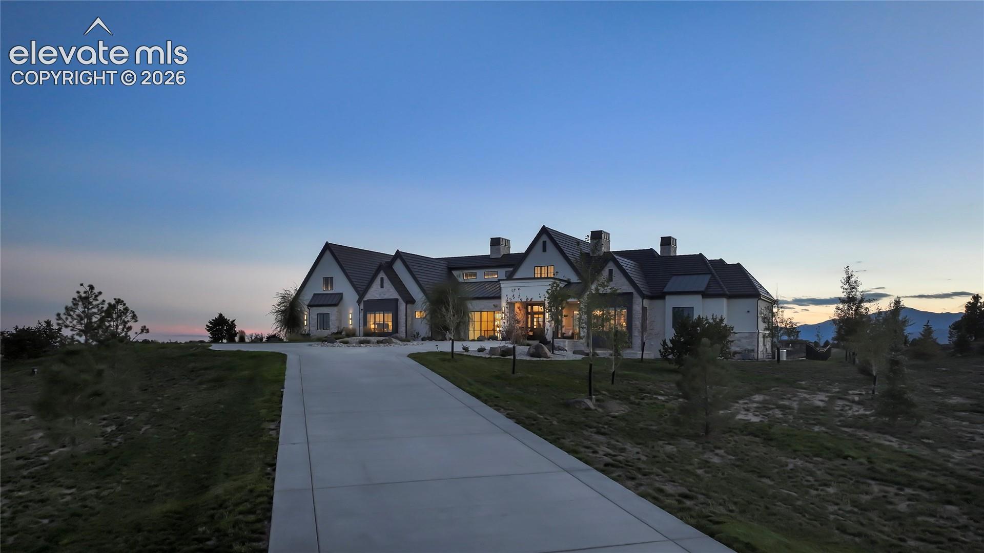 Custom estate featuring light-toned masonry exterior, multi-gabled roofline, concrete driveway, and expansive mountain scenery