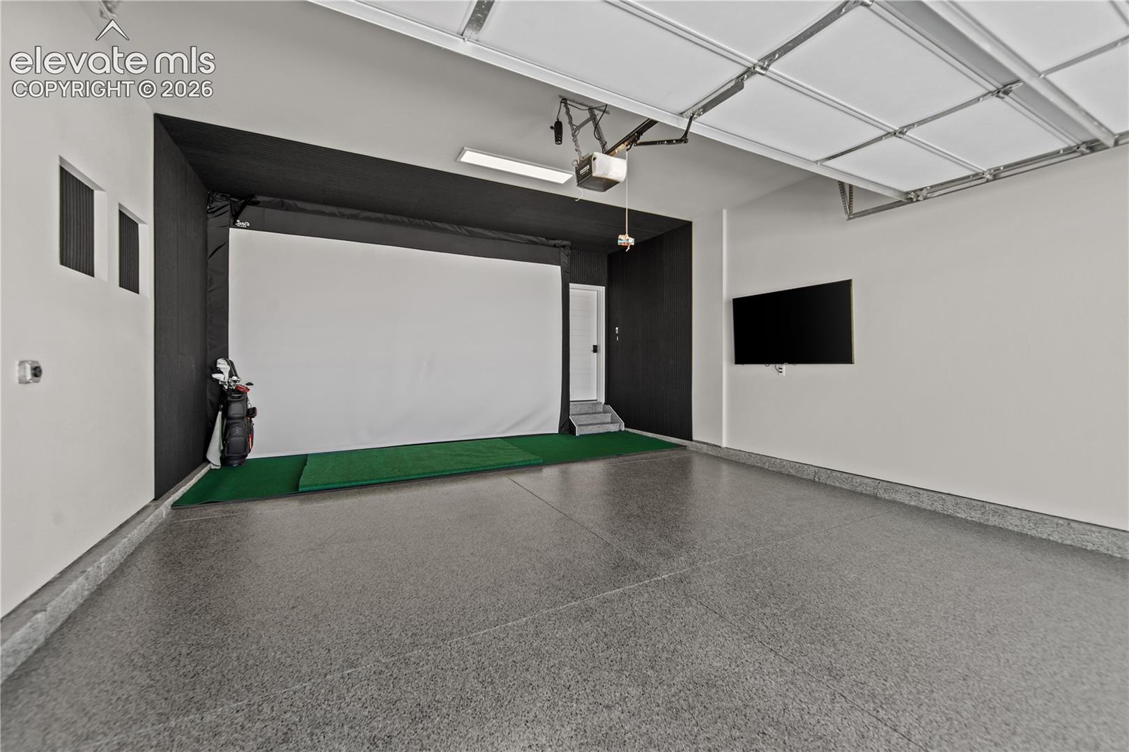 Garage space featuring finished epoxy flooring, high-contrast dark accent walls, integrated projection screen, and wall-mounted television