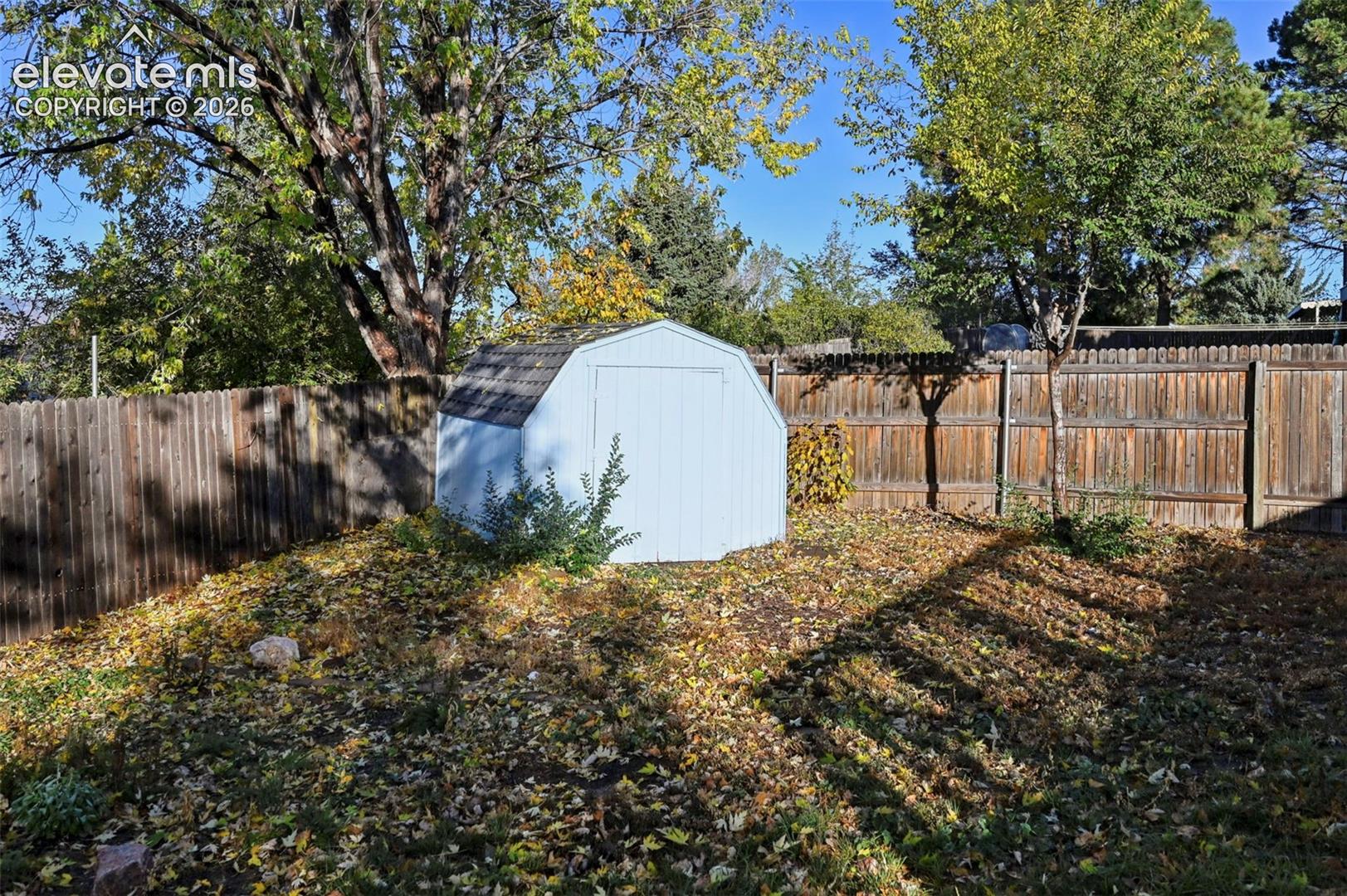 Backyard featuring a gambrel-style storage shed, wood-plank perimeter fencing, and mature trees