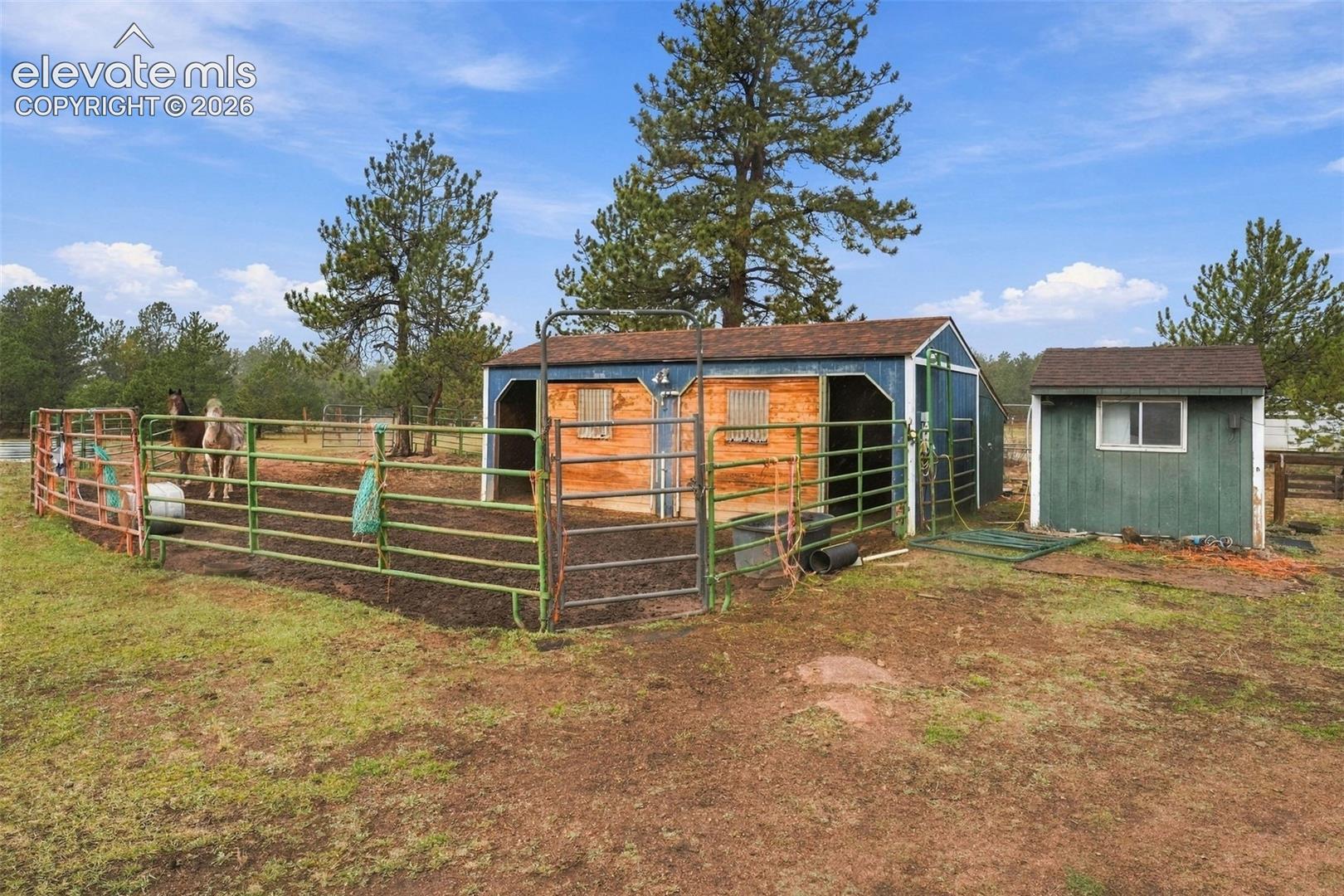 Equestrian facility featuring a multi-stall barn, metal perimeter fencing, an open-air paddock, and an auxiliary storage structure