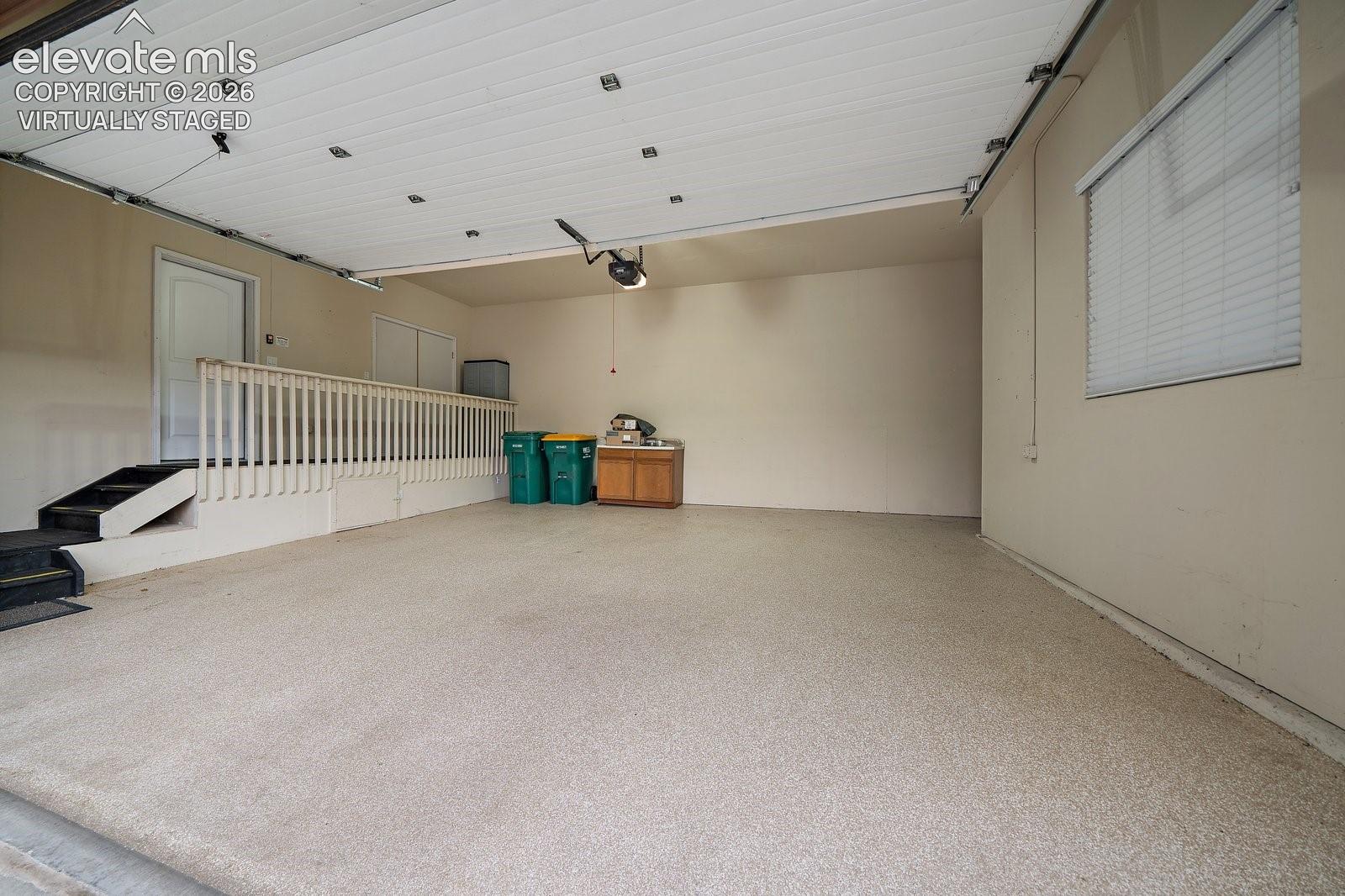 Virtually Staged. Finished garage featuring an epoxy-coated floor, built-in cabinetry, interior stairway with a wooden railing, and a window with fitted blinds