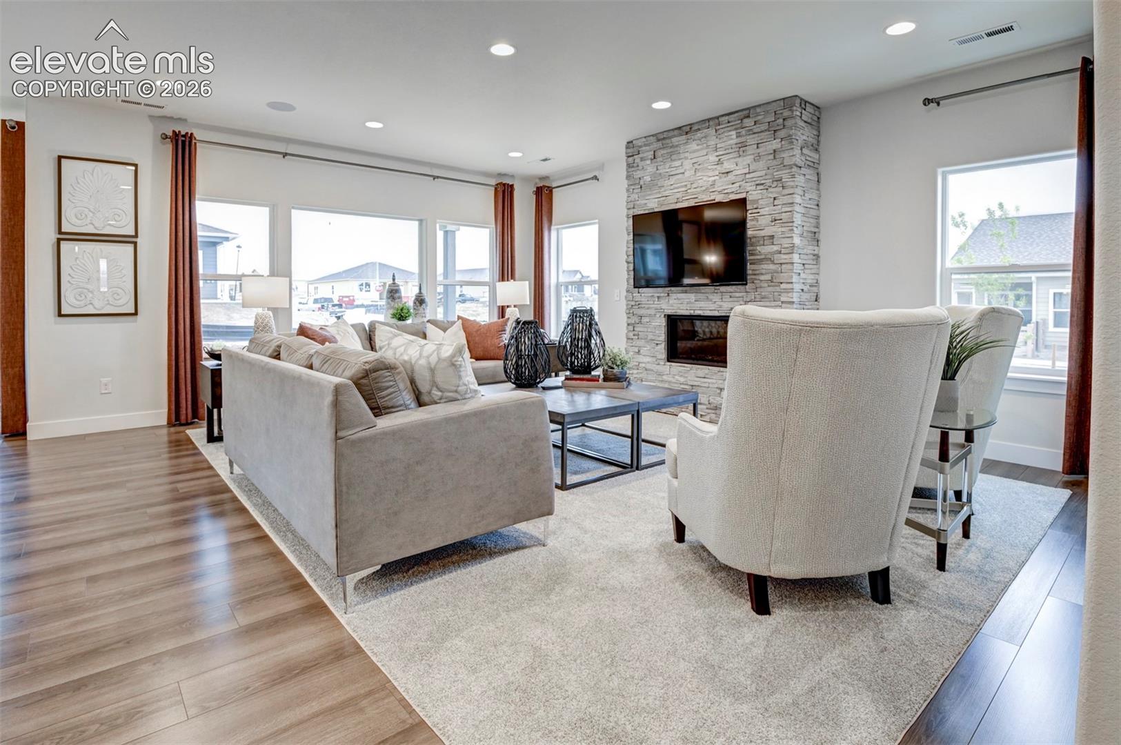 Wood-finish flooring, recessed lighting, expansive windows, a stacked stone fireplace with an integrated linear fireplace, and a television recess