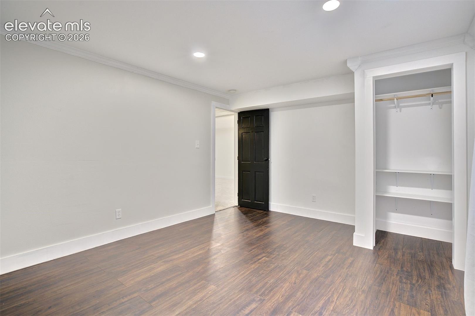 Room interior featuring wood-finish flooring, recessed lighting, crown molding, a built-in closet with shelving and a hanging rod, and a six-panel door
