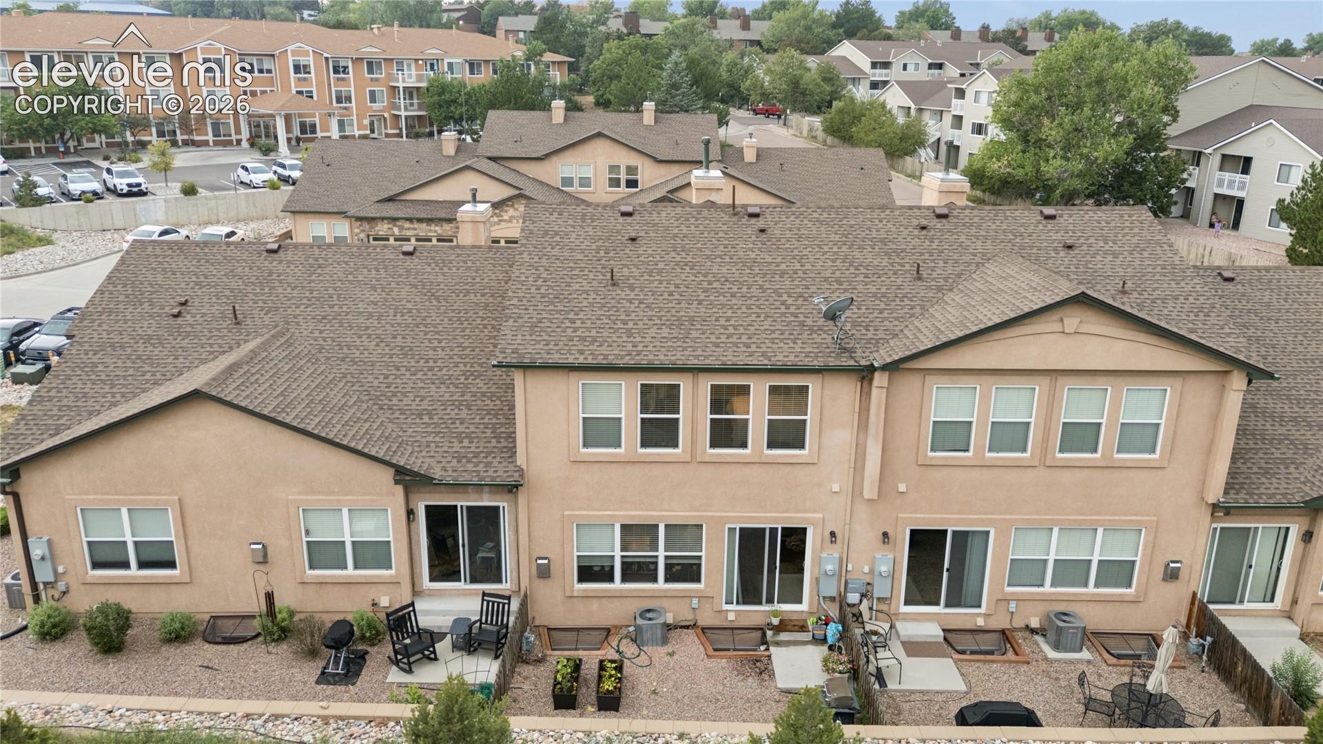 Rear exterior of multi-level townhome featuring a stucco facade and a shingled roof