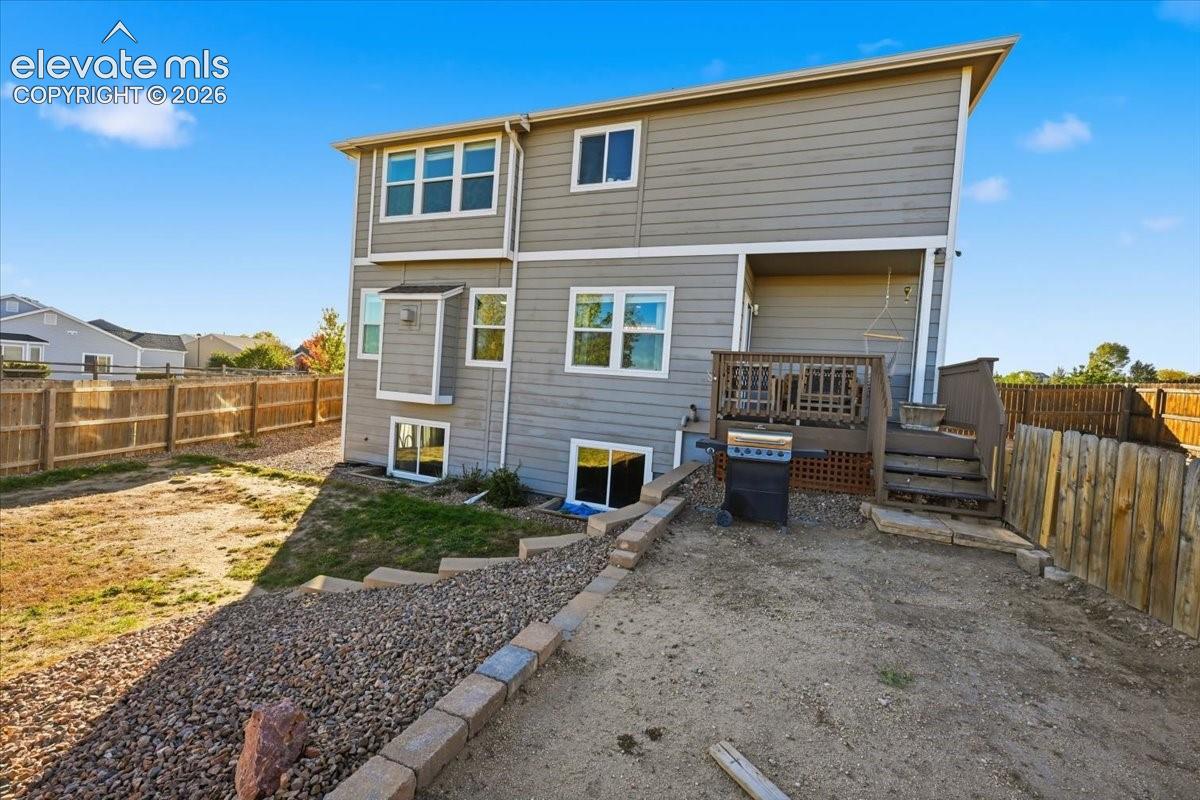 Two-story residence featuring horizontal siding, a raised wood deck, stone-block retaining walls, and perimeter wood fencing