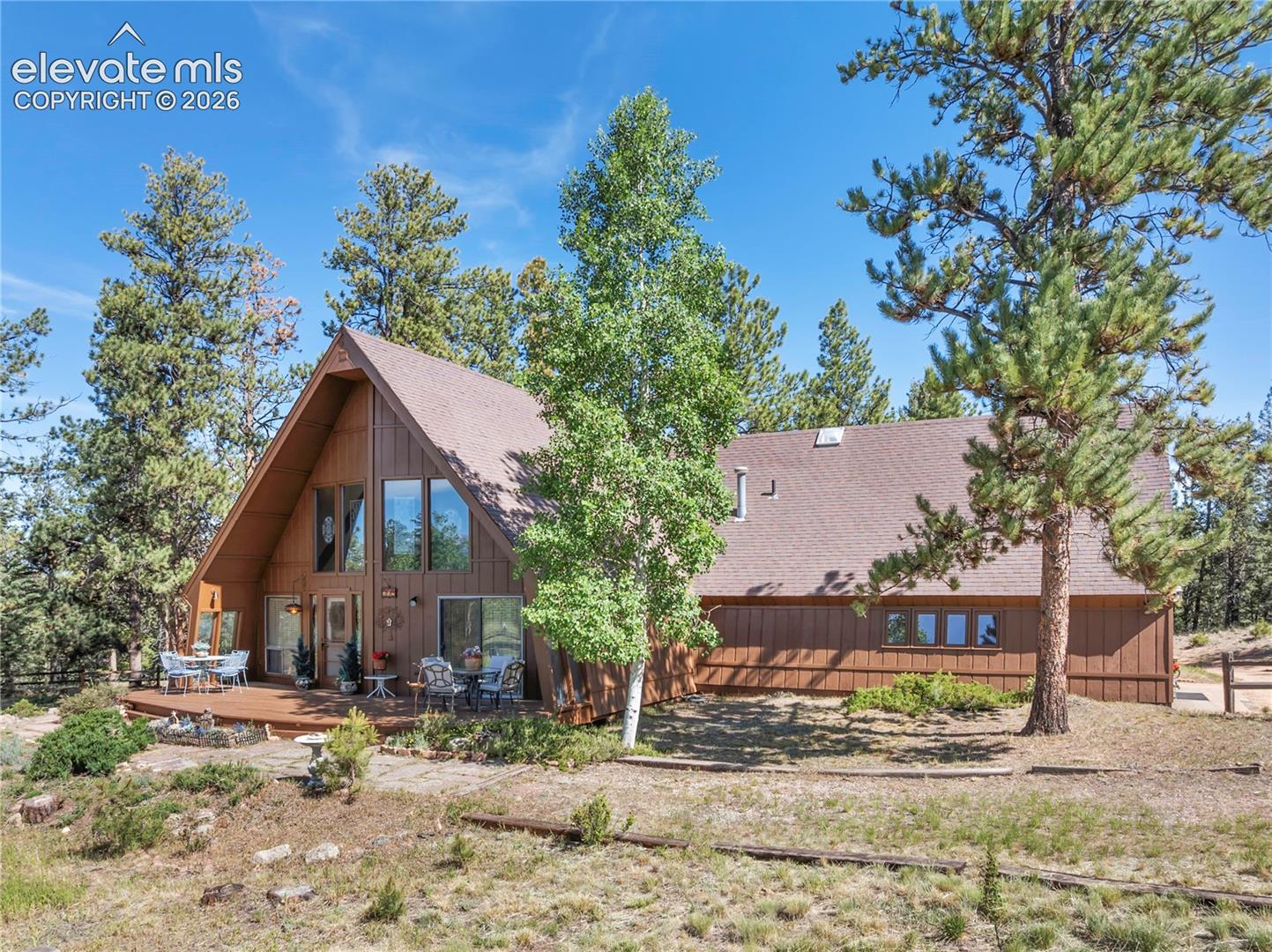 Nestled on 4 wooded acres bordering Pike National Forest, this charming chalet-style home offers the authentic Colorado mountain lifestyle buyers dream of. Set on rare, level and highly usable acreage, the property enjoys breathtaking Pikes Peak views, towering pines, beautiful aspens, abundant wildlife and direct access to hiking trails just beyond your backyard. A circular driveway welcomes you home, while the peaceful setting feels wonderfully secluded yet remains just minutes from town.Inside, the home's distinctive chalet design showcases soaring vaulted wood-beamed ceilings, expansive windows and an open-concept Great Room that seamlessly connects the living room, dining area and kitchen with breakfast bar, all centered around a cozy fireplace. Natural light pours in, framing the spectacular mountain scenery and bringing the outdoors into every season.The home features two spacious bedrooms and two full bathrooms. The main-level primary suite is tucked behind a custom architectural bookcase, creating a unique and memorable design element. Upstairs, the loft serves as a private second bedroom and bath, complete with its own balcony overlooking the surrounding forest.Additional living space includes a second rustic-style Great Room offering a comfortable TV area, game space, office nook and sunroom. Two generous decks provide the perfect setting for entertaining, grilling or simply enjoying the peaceful mountain surroundings. The property also includes an attached one-car garage, a detached two-car garage and abundant guest parking.Located just 10 minutes from Woodland Park and 30 minutes from Colorado Springs, you'll enjoy the privacy of mountain living without sacrificing convenient access to shopping, dining and everyday amenities.If you've been searching for an authentic mountain retreat with usable acreage, National Forest access, stunning views and timeless Colorado character, this exceptional property is ready to welcome you home.