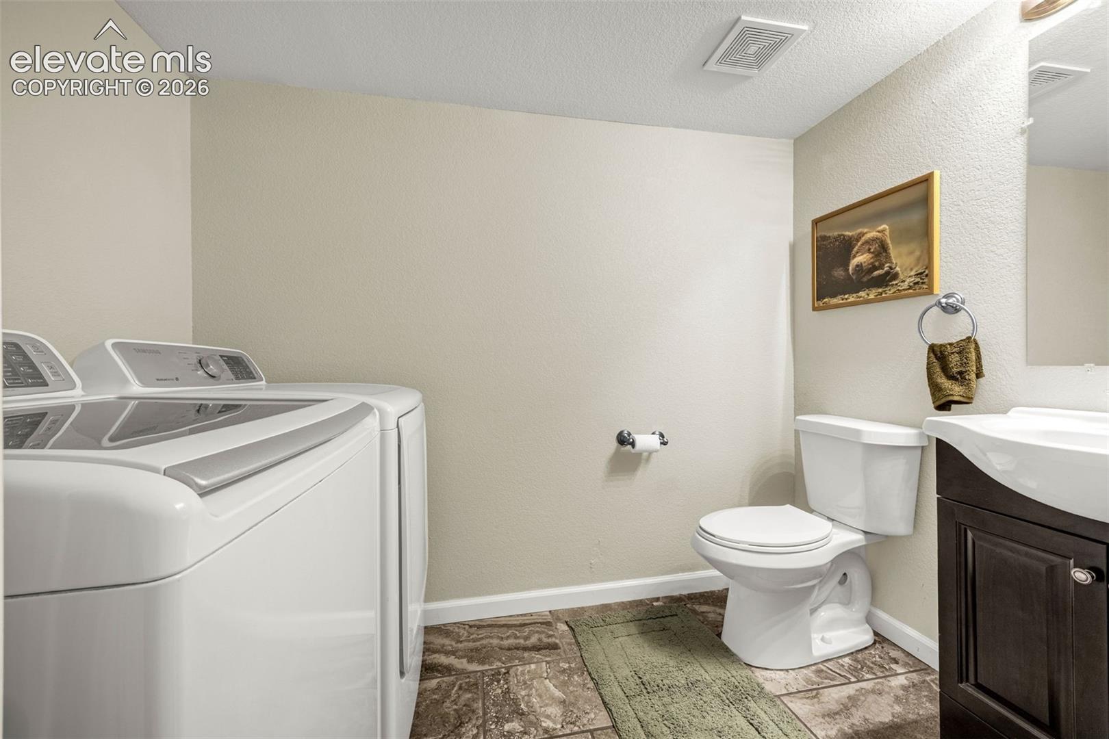 Laundry area featuring stone-patterned tile flooring, a dark wood-finish vanity with a white integrated sink, and a porcelain toilet