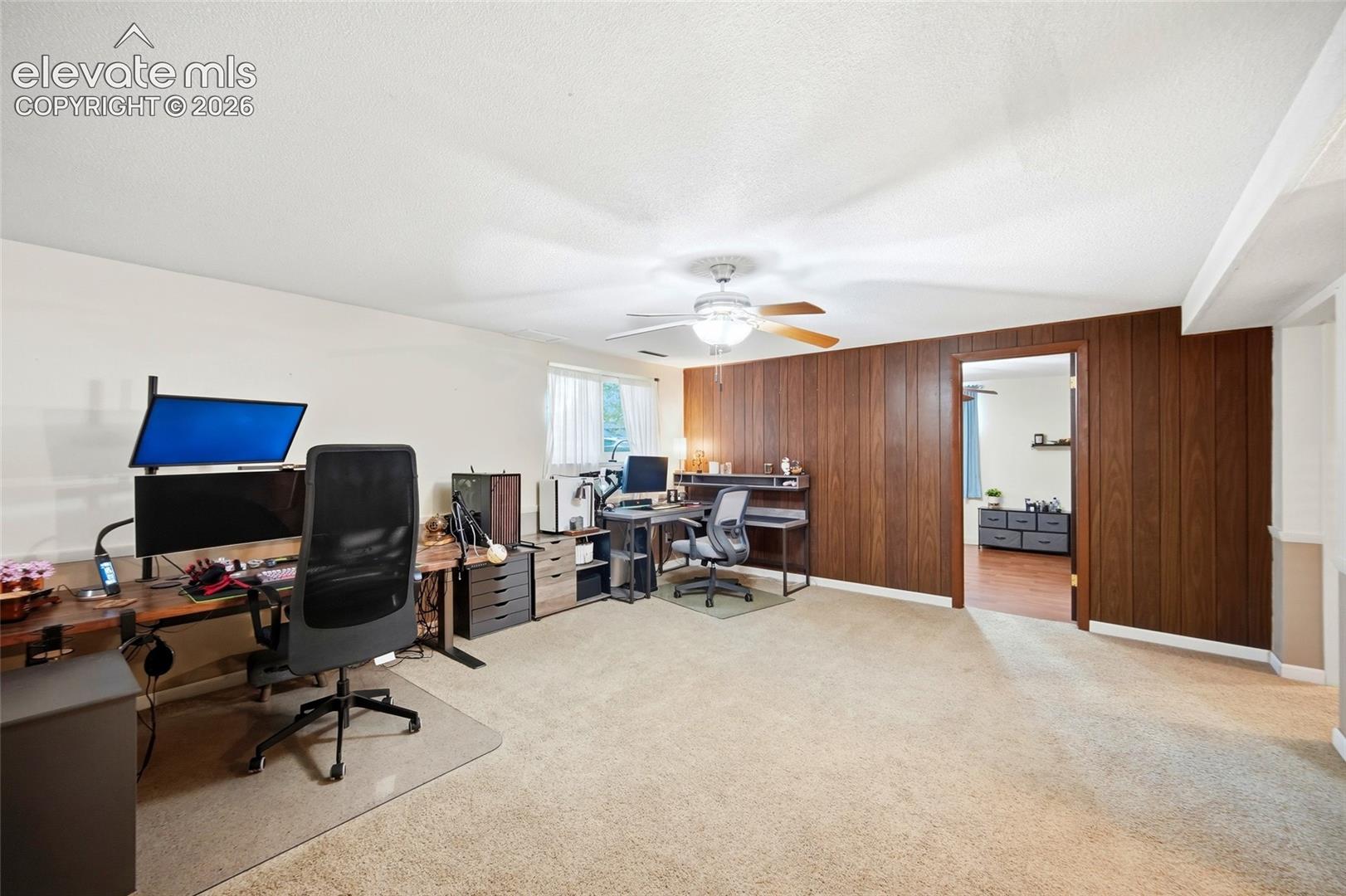 Neutral-toned carpeting, wood-paneled feature wall, ceiling-mounted light fixture with fan, and natural light from a single window