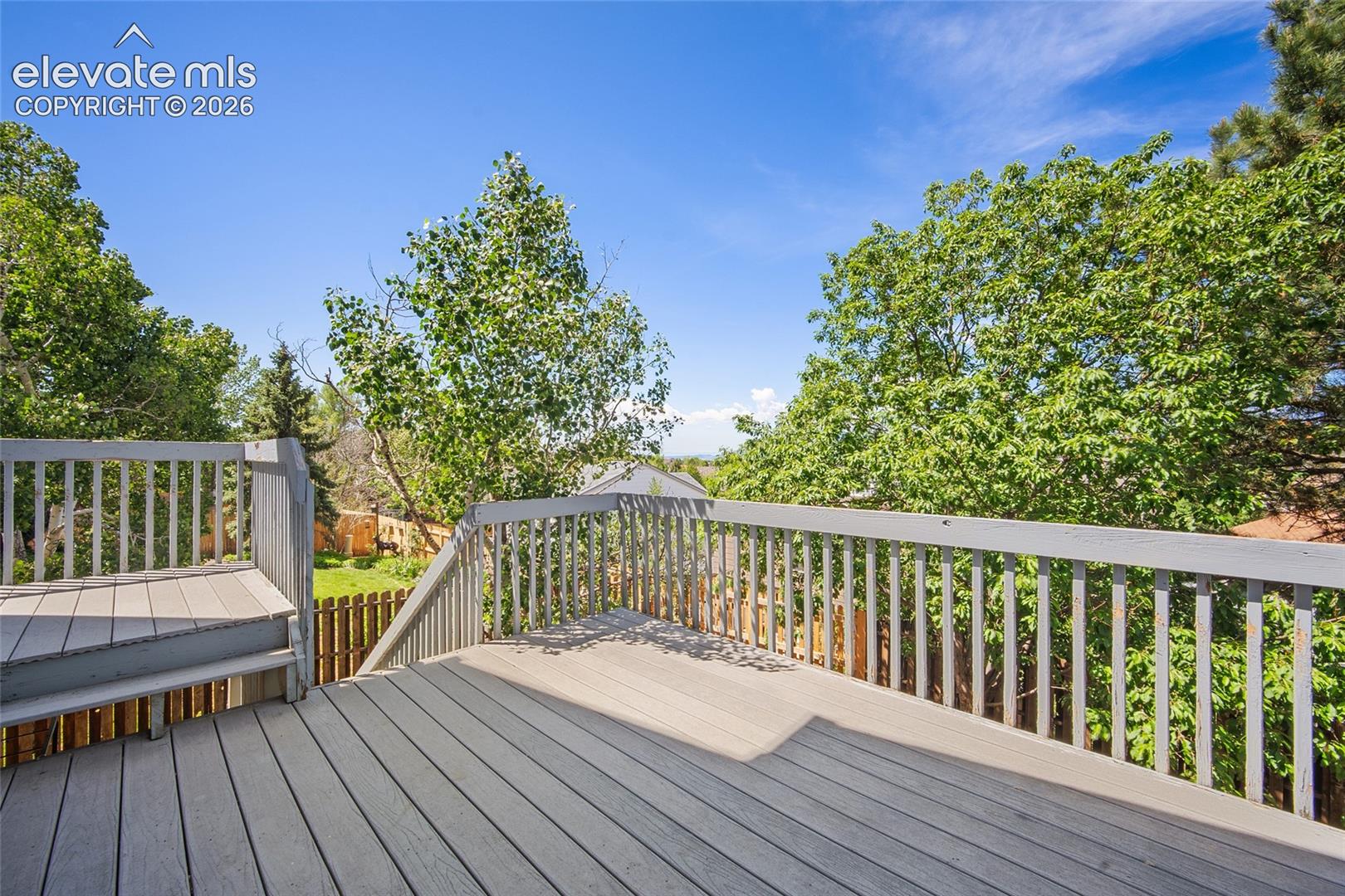 Spacious composite deck with sturdy railings, integrated steps, and surrounding mature trees