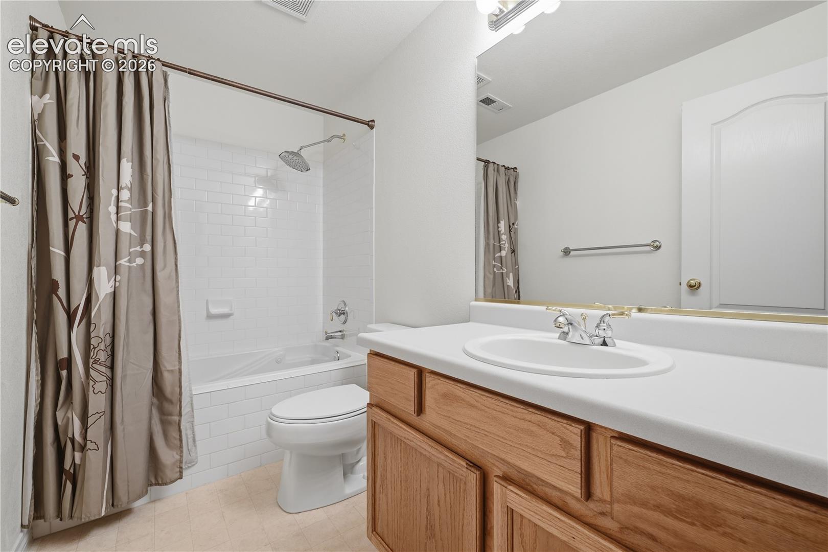 Bathroom featuring a wood-finish vanity with a solid-surface countertop, an integrated oval sink, a shower-tub combination with white subway tile surround, and a wall-to-wall vanity mirror