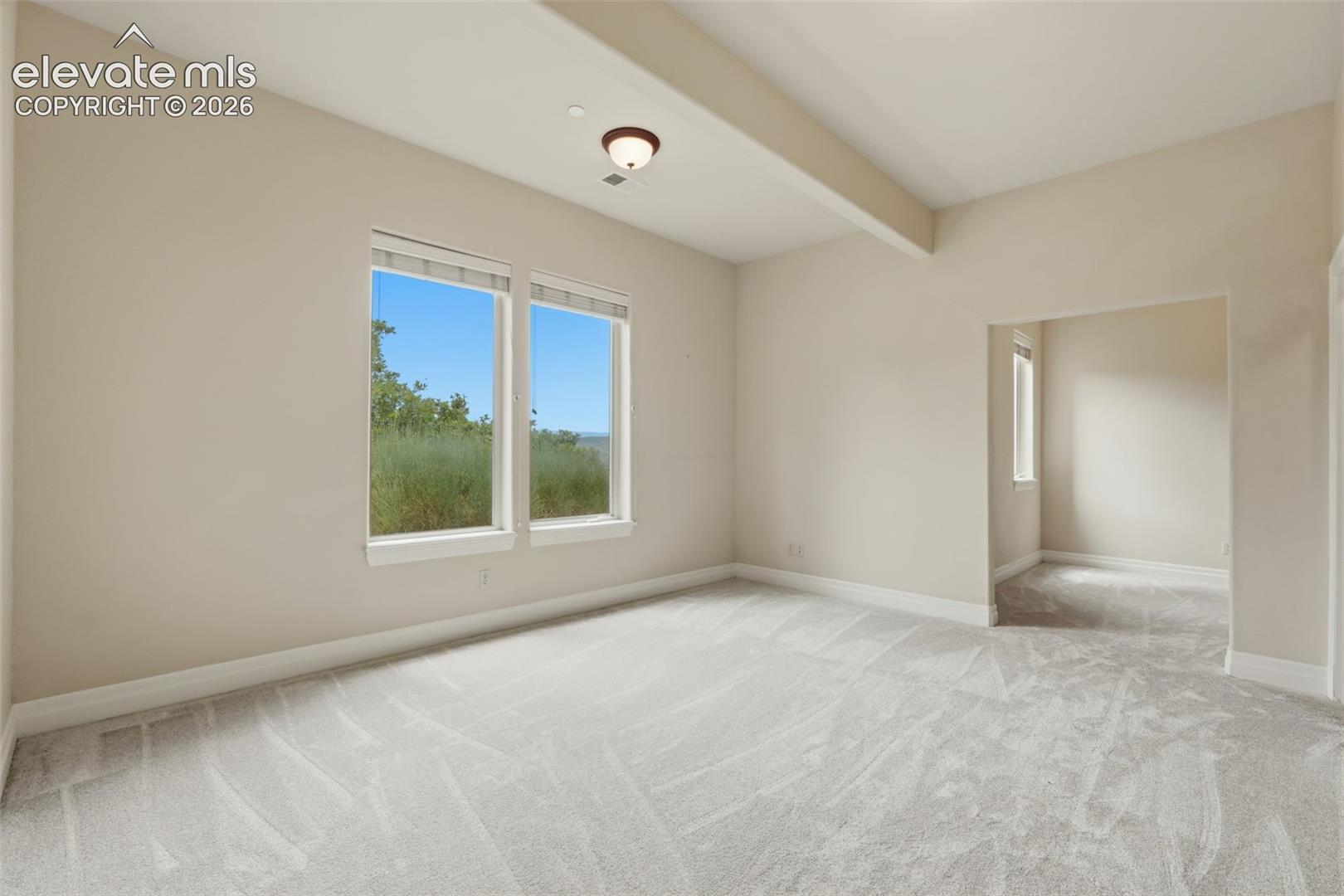 Spacious room featuring neutral carpeting, light-toned walls, and a ceiling beam detail