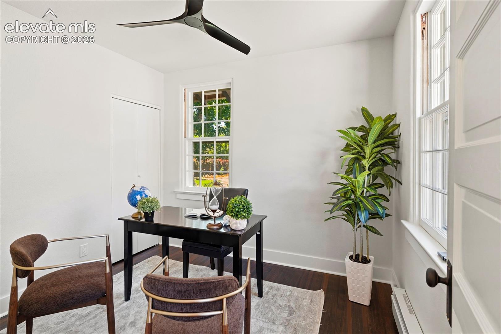 Room featuring dark wood-finish flooring, multi-pane windows, and a matte black three-blade ceiling fan