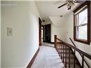 Hallway featuring wood-finish staircase railing, ceiling-mounted fan, and window with wood-trim detailing