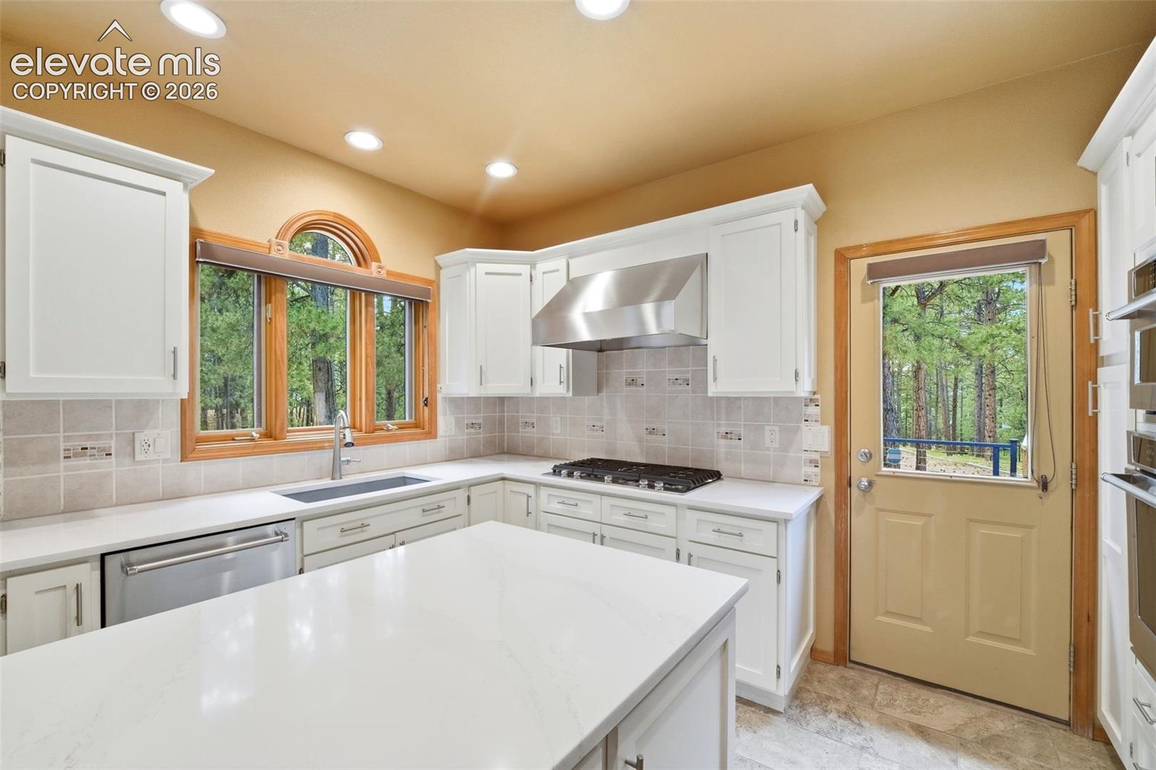 Kitchen featuring white cabinetry, light-toned countertops, tile backsplash, and recessed lighting
