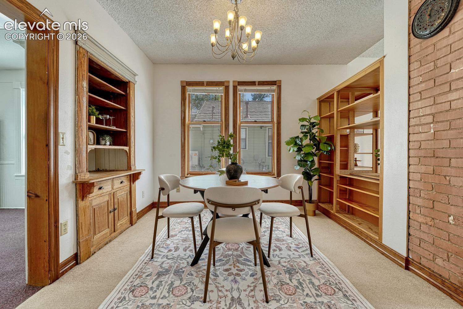 Built-in cabinetry with exposed shelving, two large windows, wood-paneled built-in shelving, and a brick accent wall