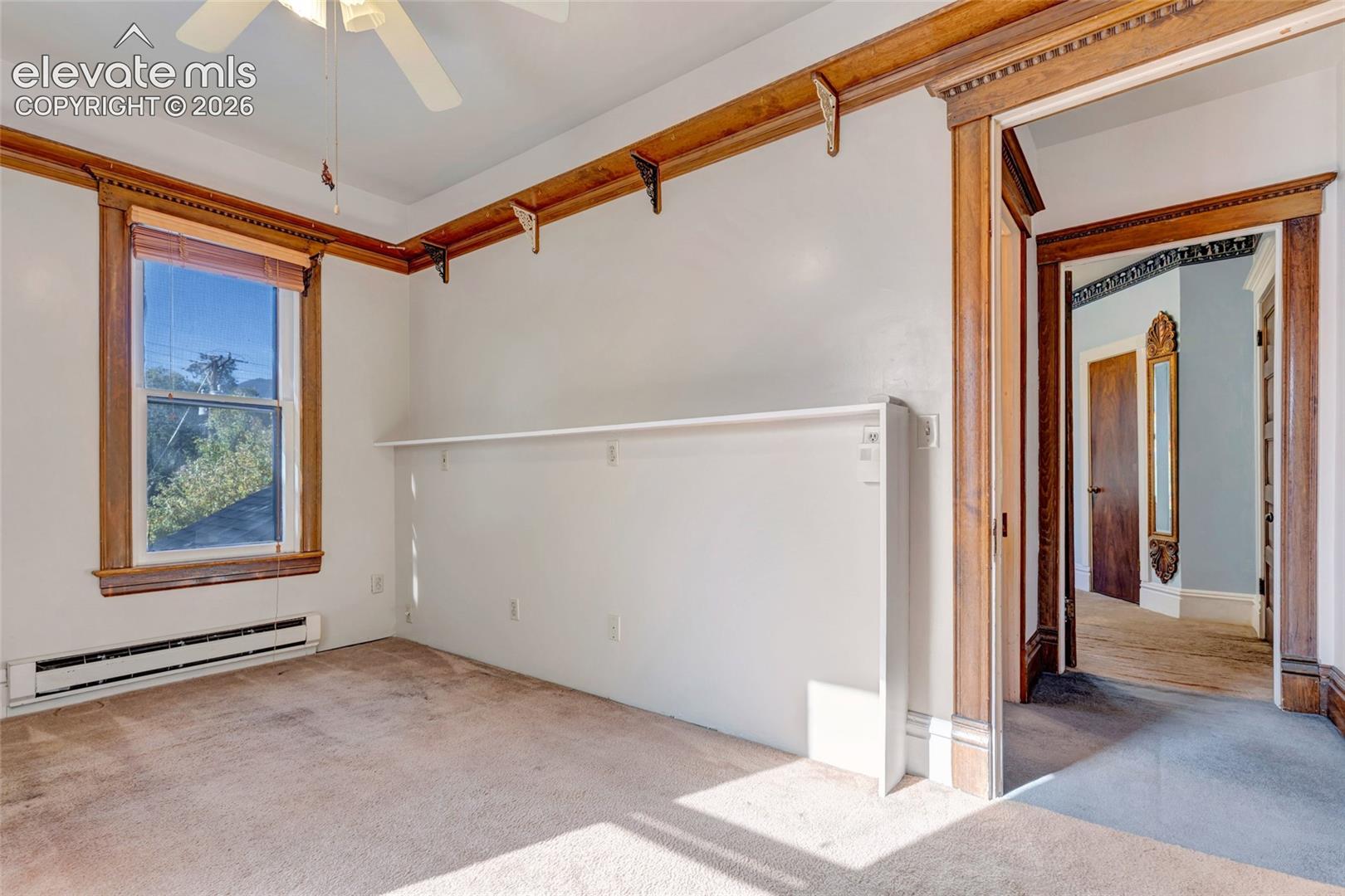 Interior space featuring stained-wood crown molding, ornamental wood trim, a built-in wall shelf, and a ceiling fan