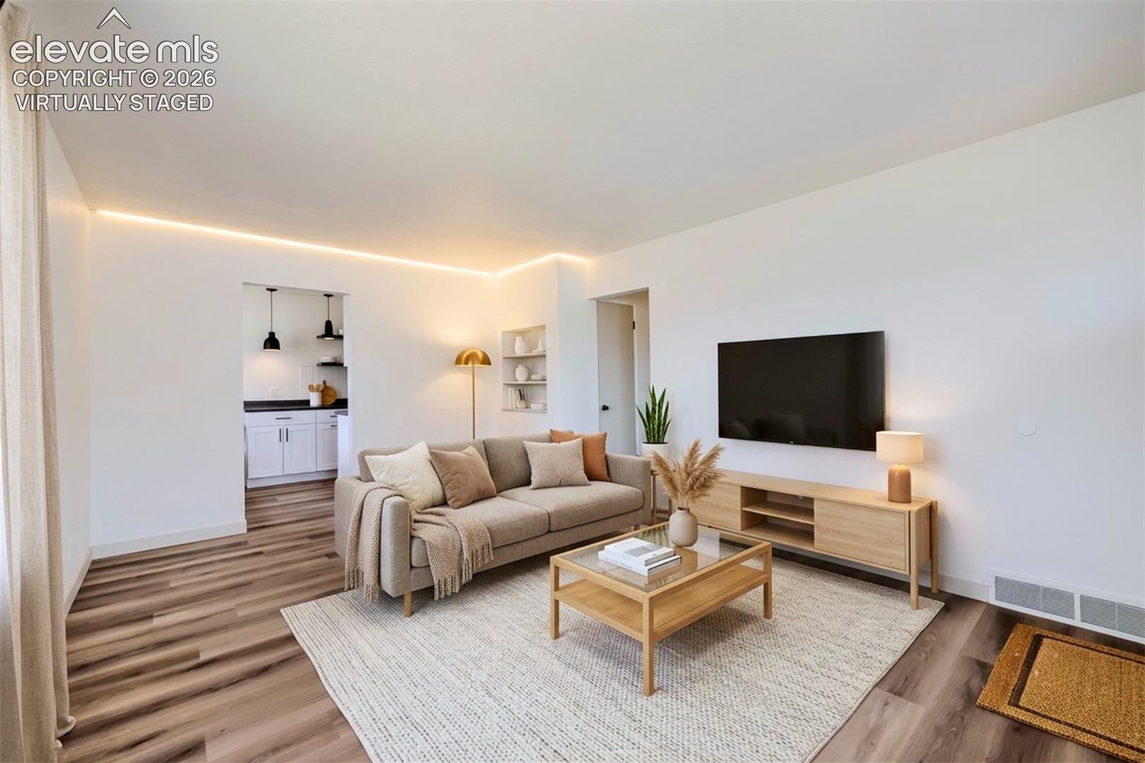 Bright living space featuring wood-finish flooring and integrated cove lighting. Virtually staged.