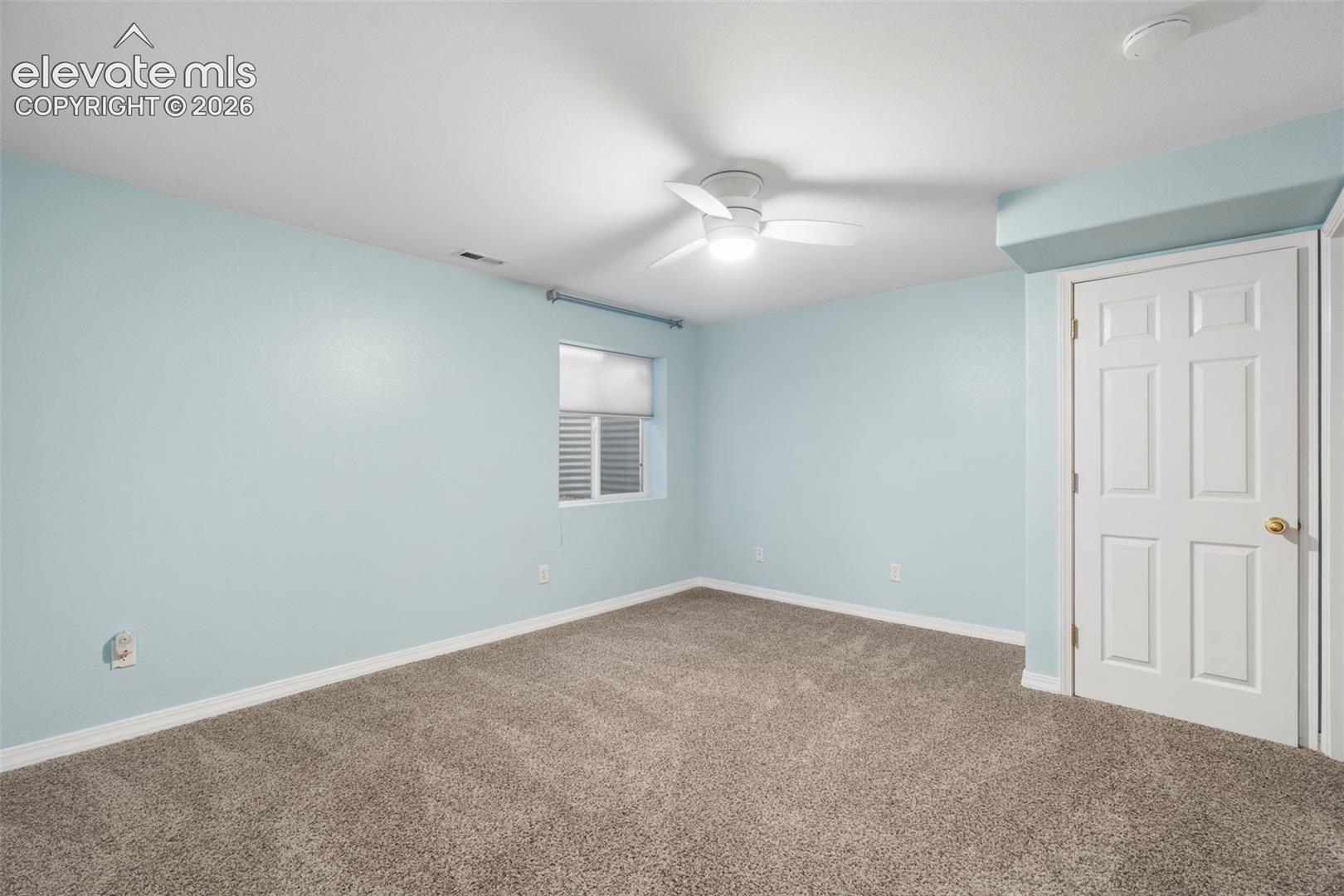 Neutral-toned wall-to-wall carpeting, white six-panel interior door, ceiling-mounted light fixture with fan, and a single-hung window with horizontal blinds