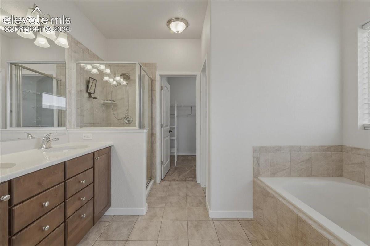 Bathroom featuring a dual vanity with a light countertop, a glass-enclosed shower, a built-in tub with tile surround, and tile flooring
