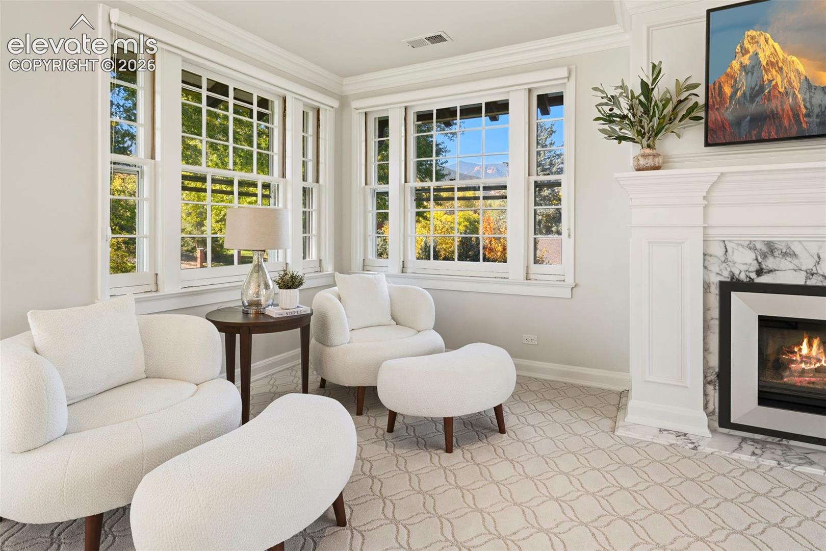 Fireplace with stone surround, crown molding, and large grid-pane windows with mountain scenery