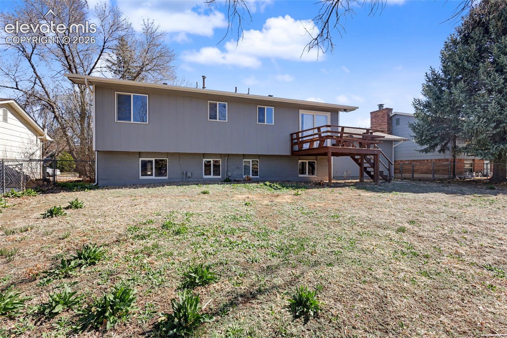 Exterior rear elevation featuring a multi-level wood deck, masonry chimney, and metal-fenced yard