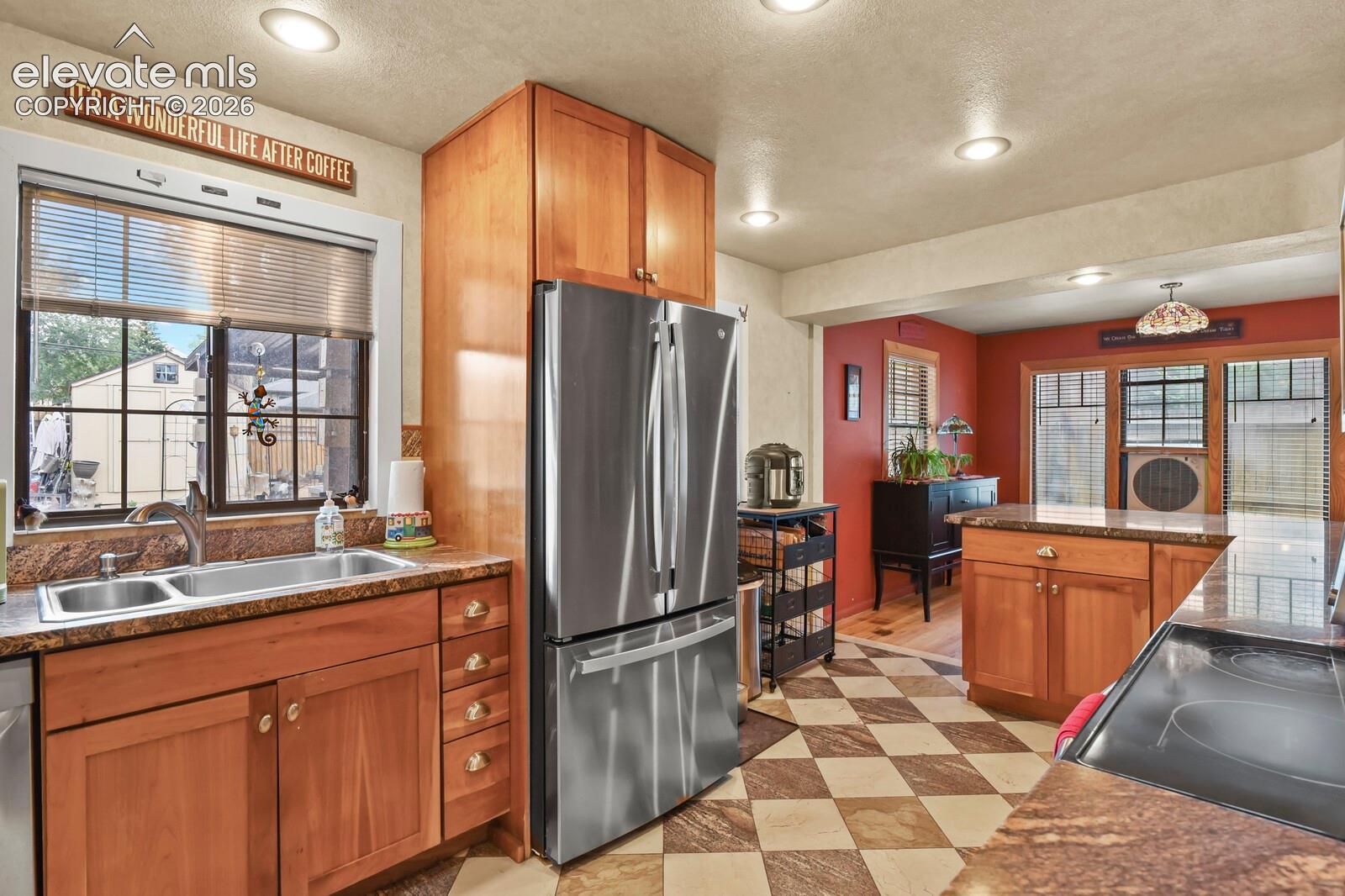 Recessed ceiling lighting, wood cabinetry, stone countertops, stainless steel appliances, and checkered tile flooring