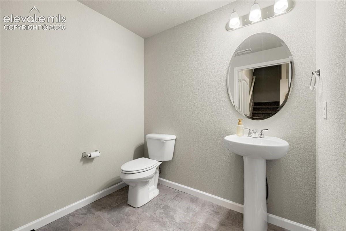 Pedestal sink with chrome faucet, oval mirror, wall-mounted light fixture, and tile flooring