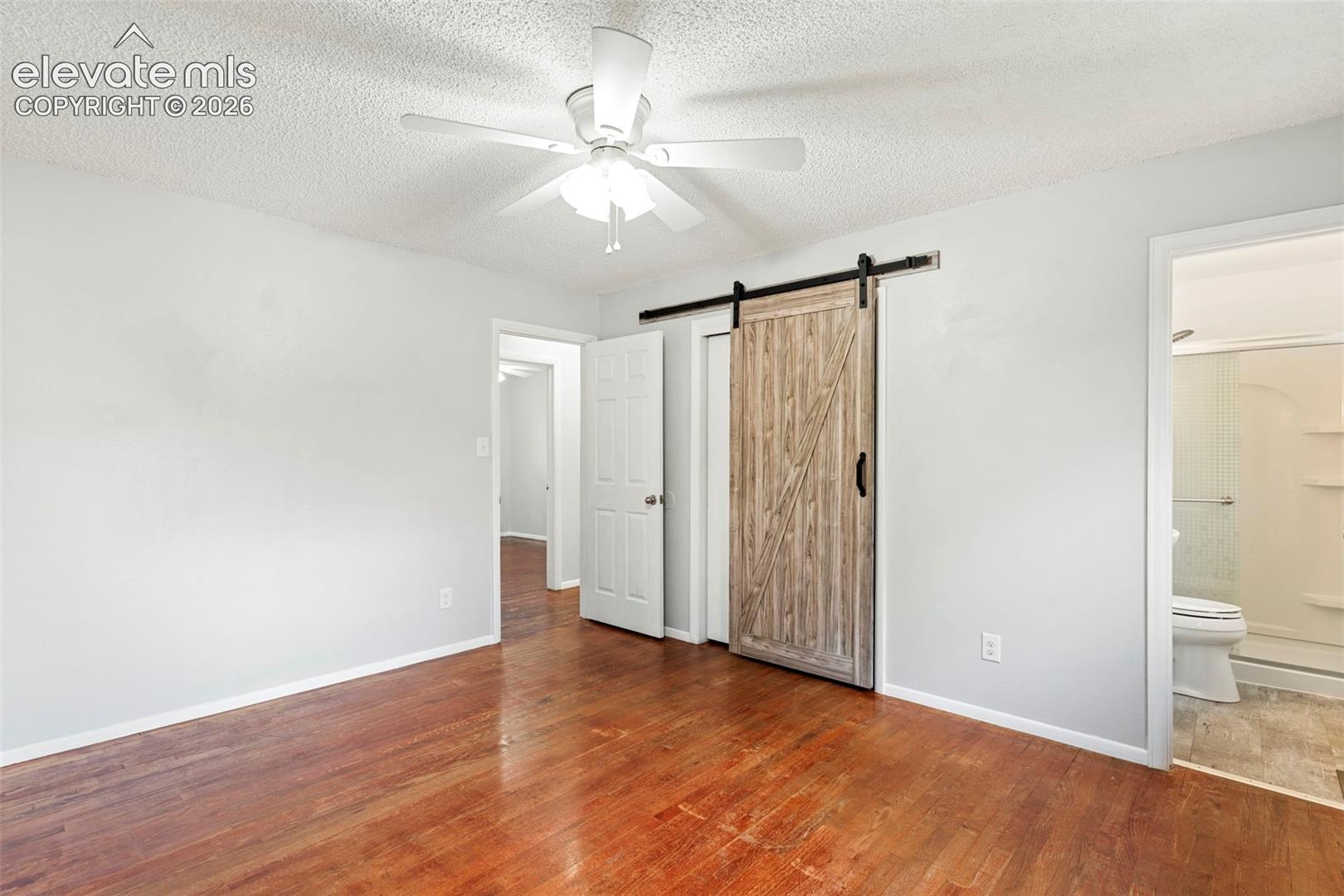 Hardwood flooring, ceiling fan with light fixture, wood-finish barn door, and a full bathroom with shower