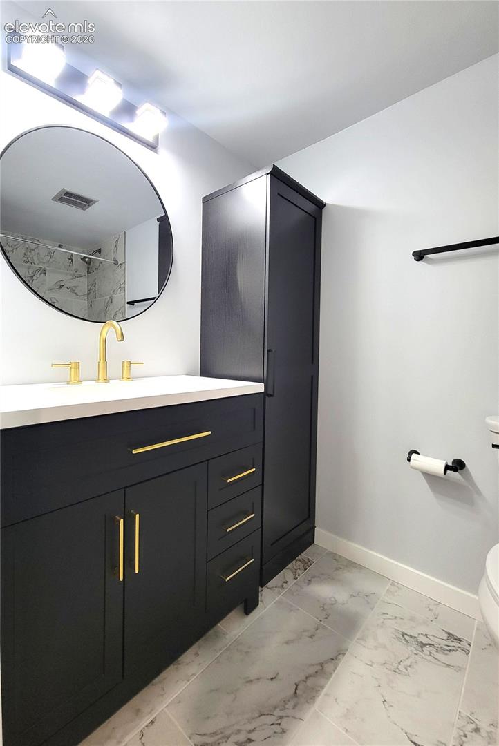 Bathroom featuring a black vanity with gold hardware, white countertop, and gold-finish faucet