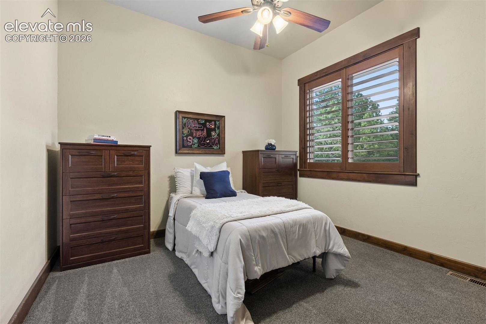 Interior room featuring high ceilings, wall-to-wall carpeting, wood-cased windows with horizontal shutters, and an integrated ceiling fan with a light fixture