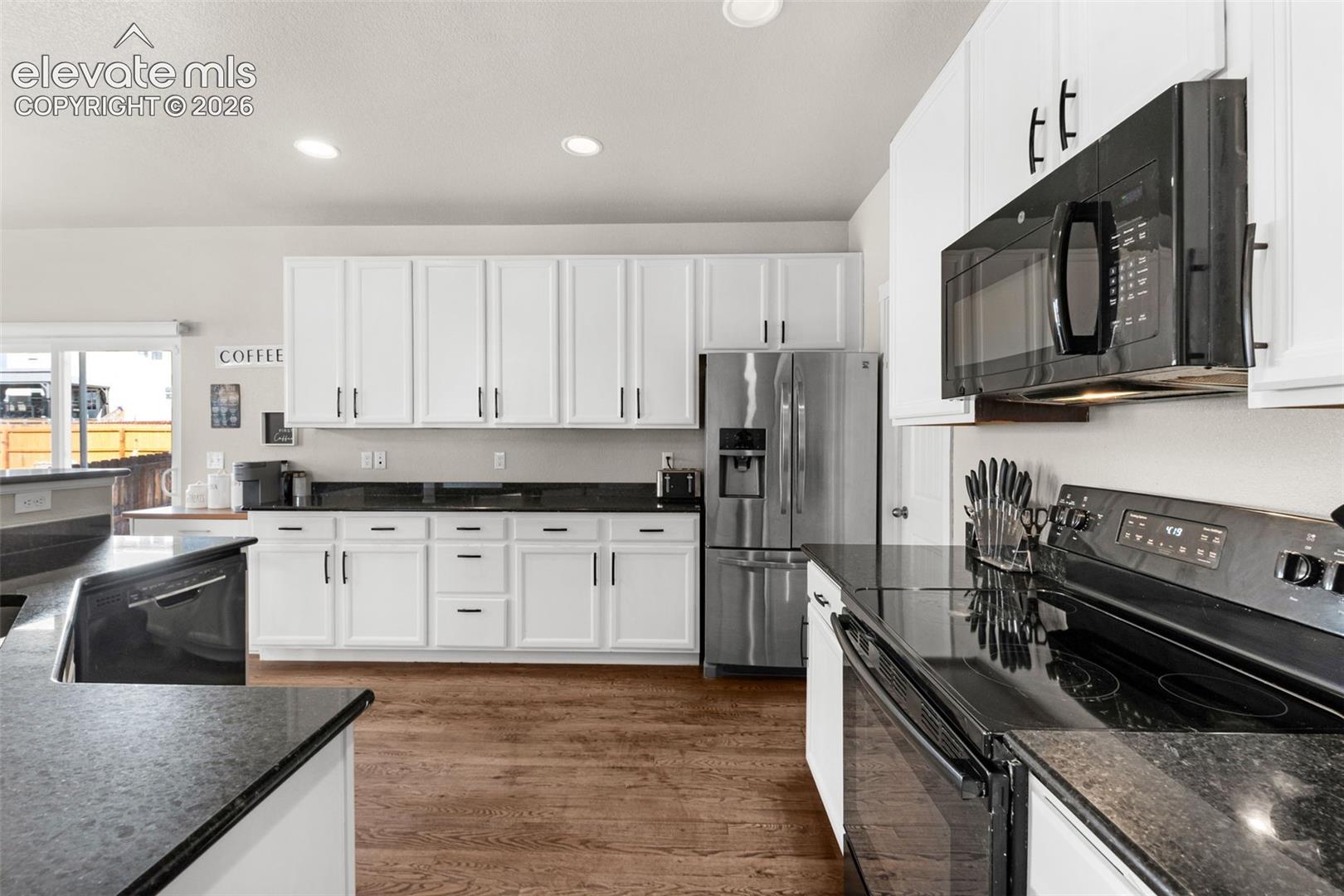 Kitchen featuring white cabinetry, dark stone countertops, wood-finish flooring, and stainless steel appliances