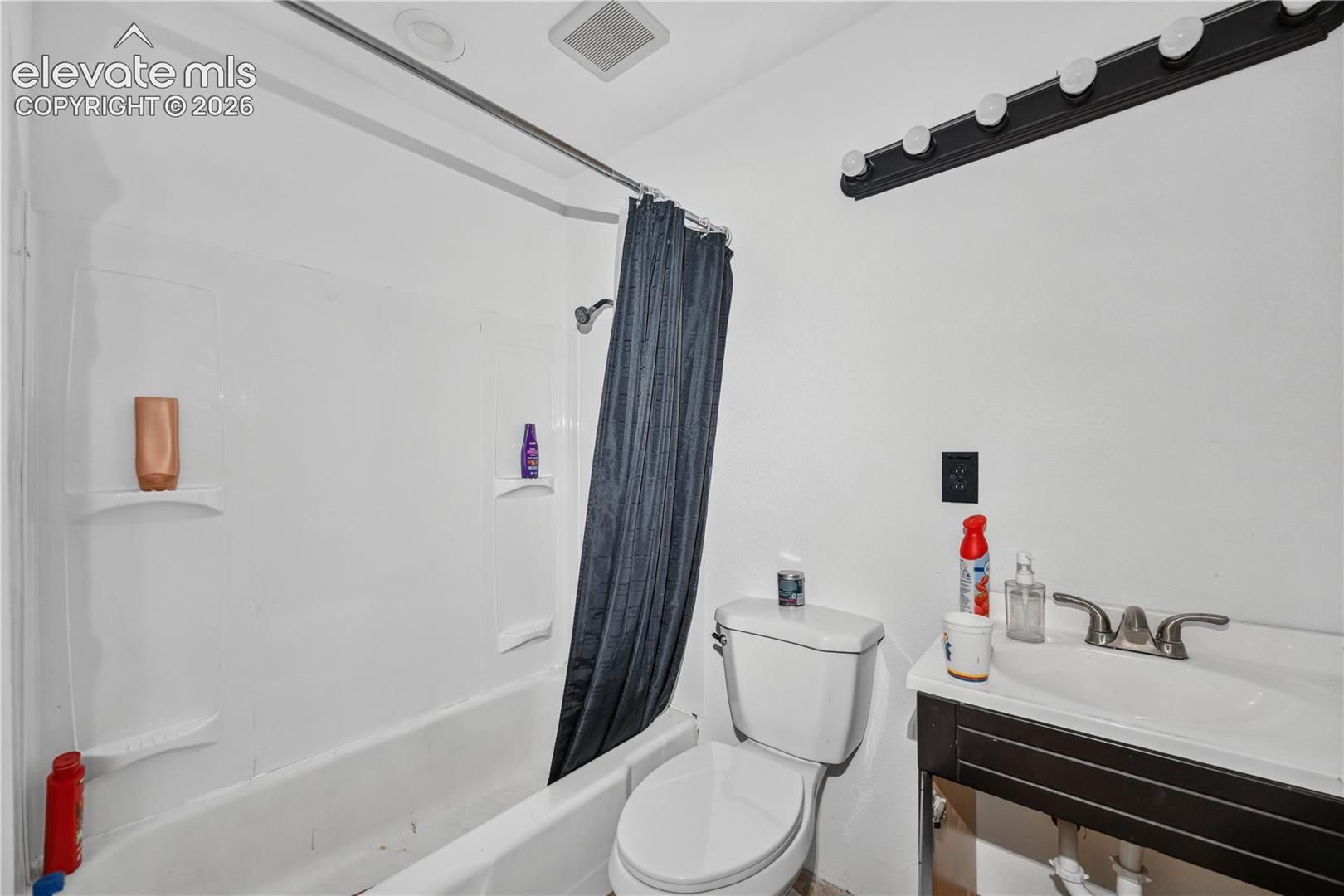 Bathroom featuring a white molded tub surround with integrated shelving, a pedestal-style vanity with a dark finish, and a multi-bulb vanity light fixture